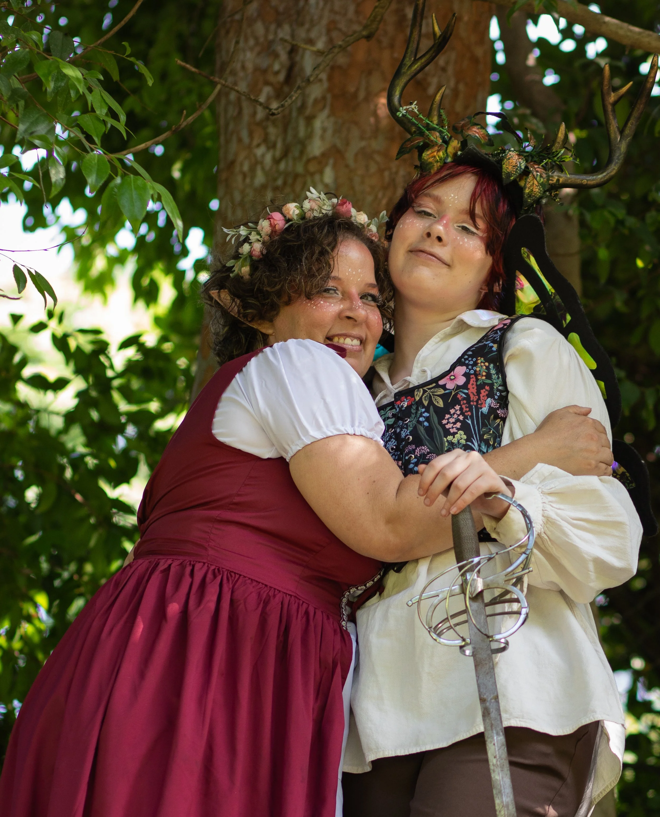 Mom and teen hugging, smiling, dressed as fairy and fae, holding a sword outdoors. Fantasy family photographer in hesperia, ca.