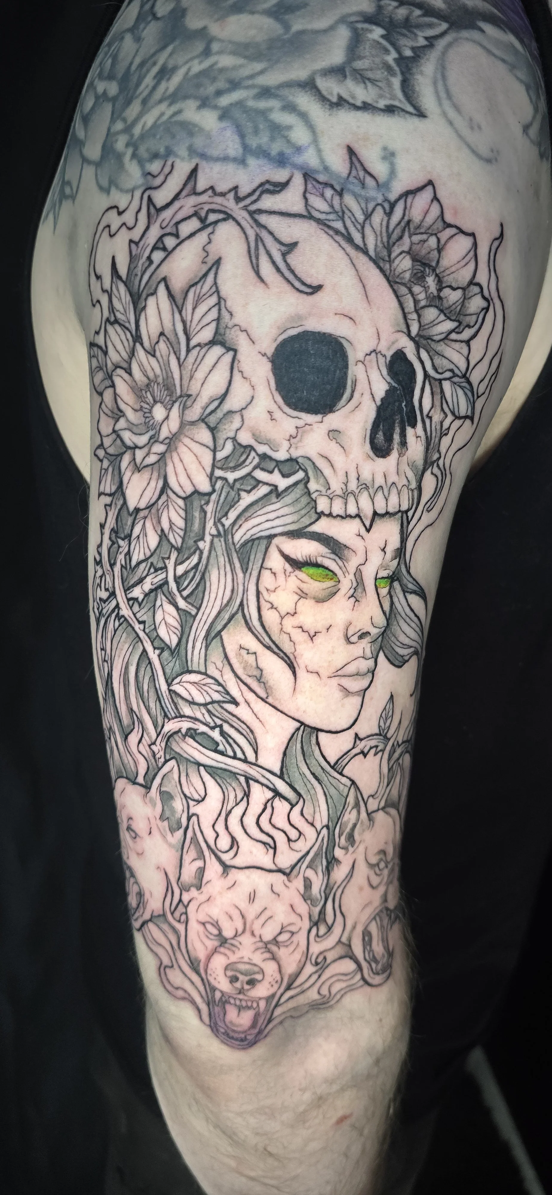 Tattoo of a woman with green eyes, surrounded by a skull, a wolf, flowers, and vines.