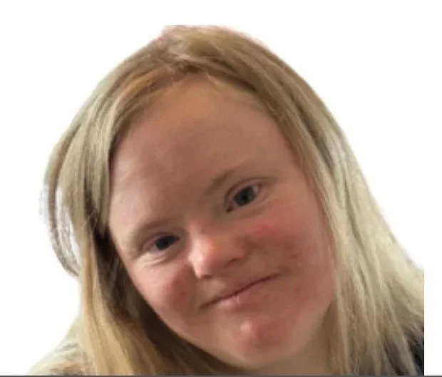 A young girl with long blonde hair smiling at the camera, wearing a black t-shirt with a logo on the front.