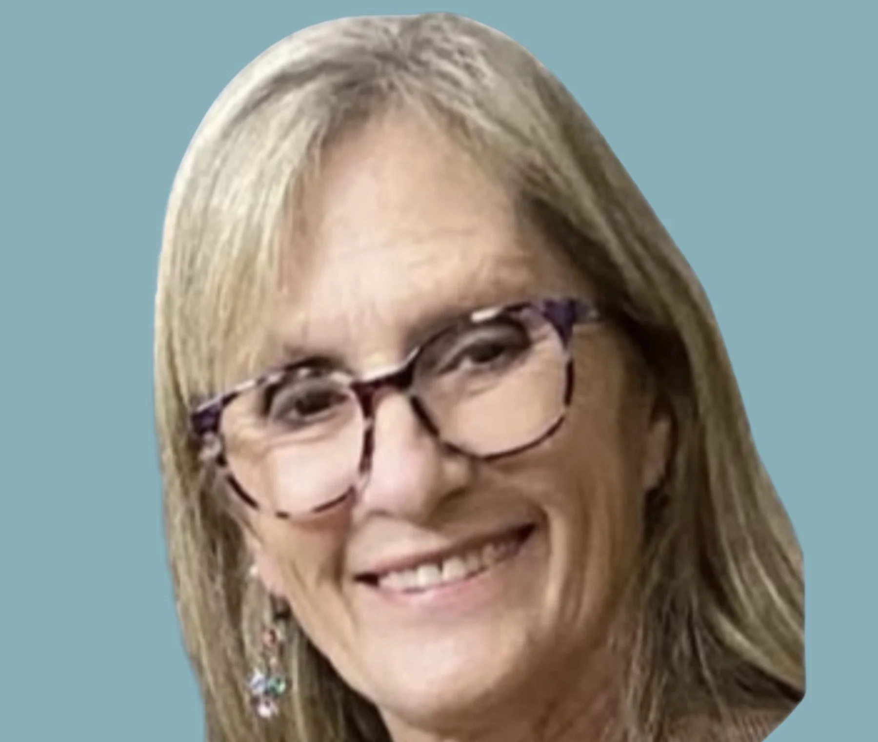 A smiling woman with short blonde hair, glasses, and a white T-shirt with a floral pattern, standing indoors.