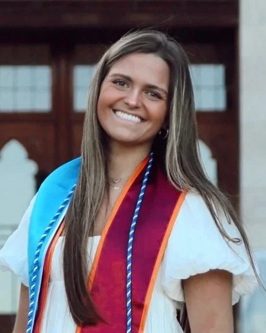 Young woman in graduation gown smiling outdoors.