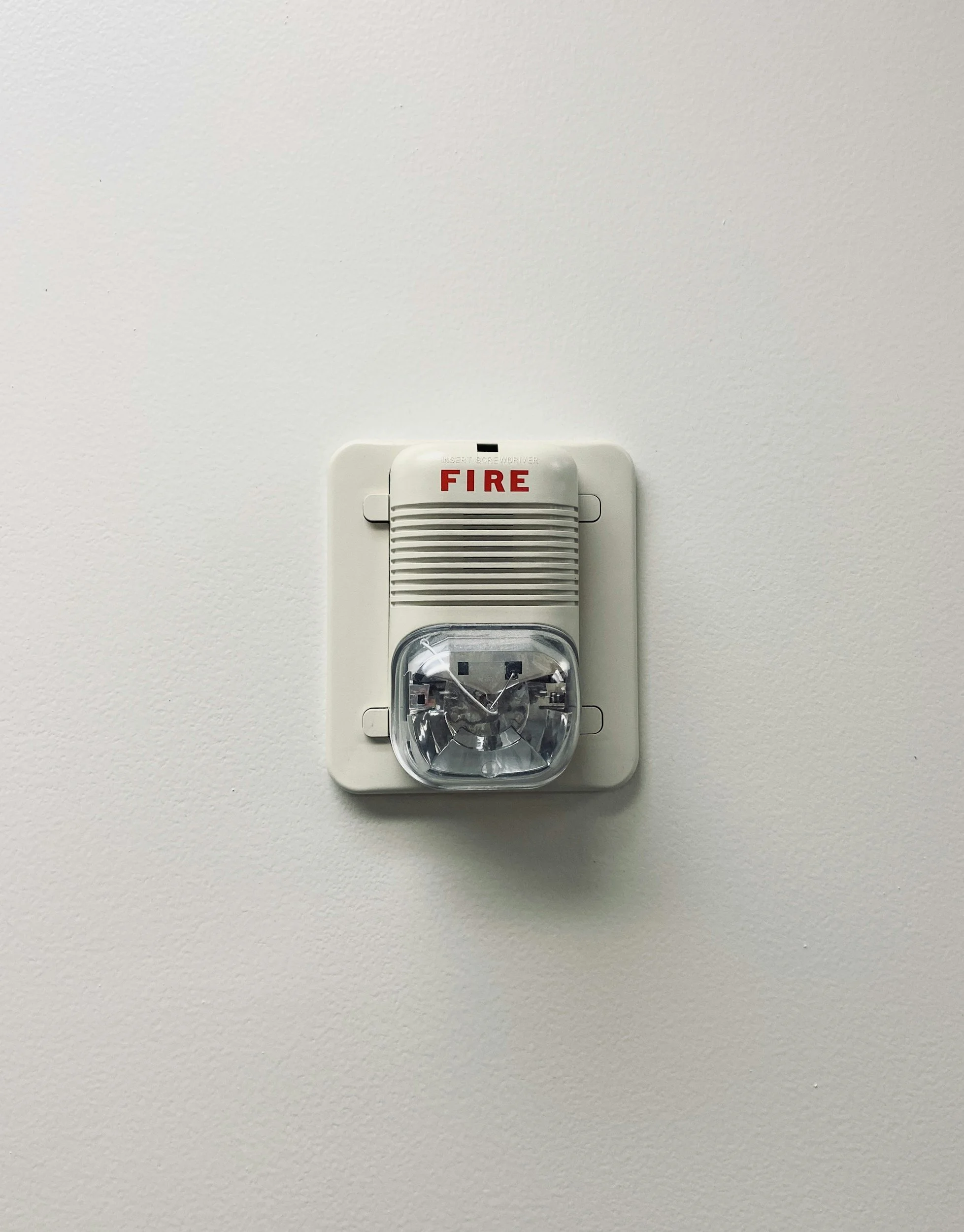 White wall-mounted fire alarm with a red 'FIRE' label and a clear siren cover.