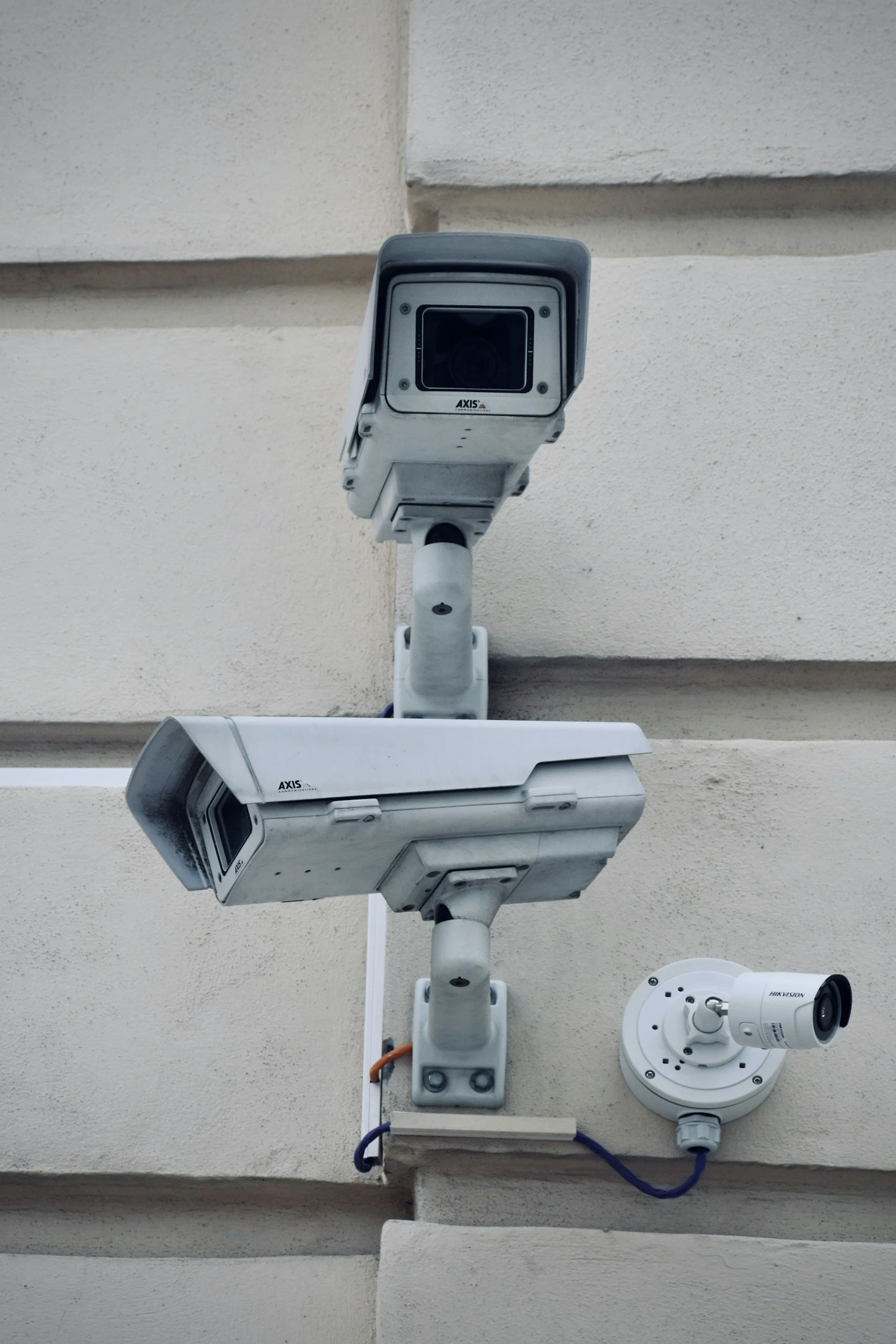 Three security cameras mounted on a beige exterior wall, facing different directions for surveillance.