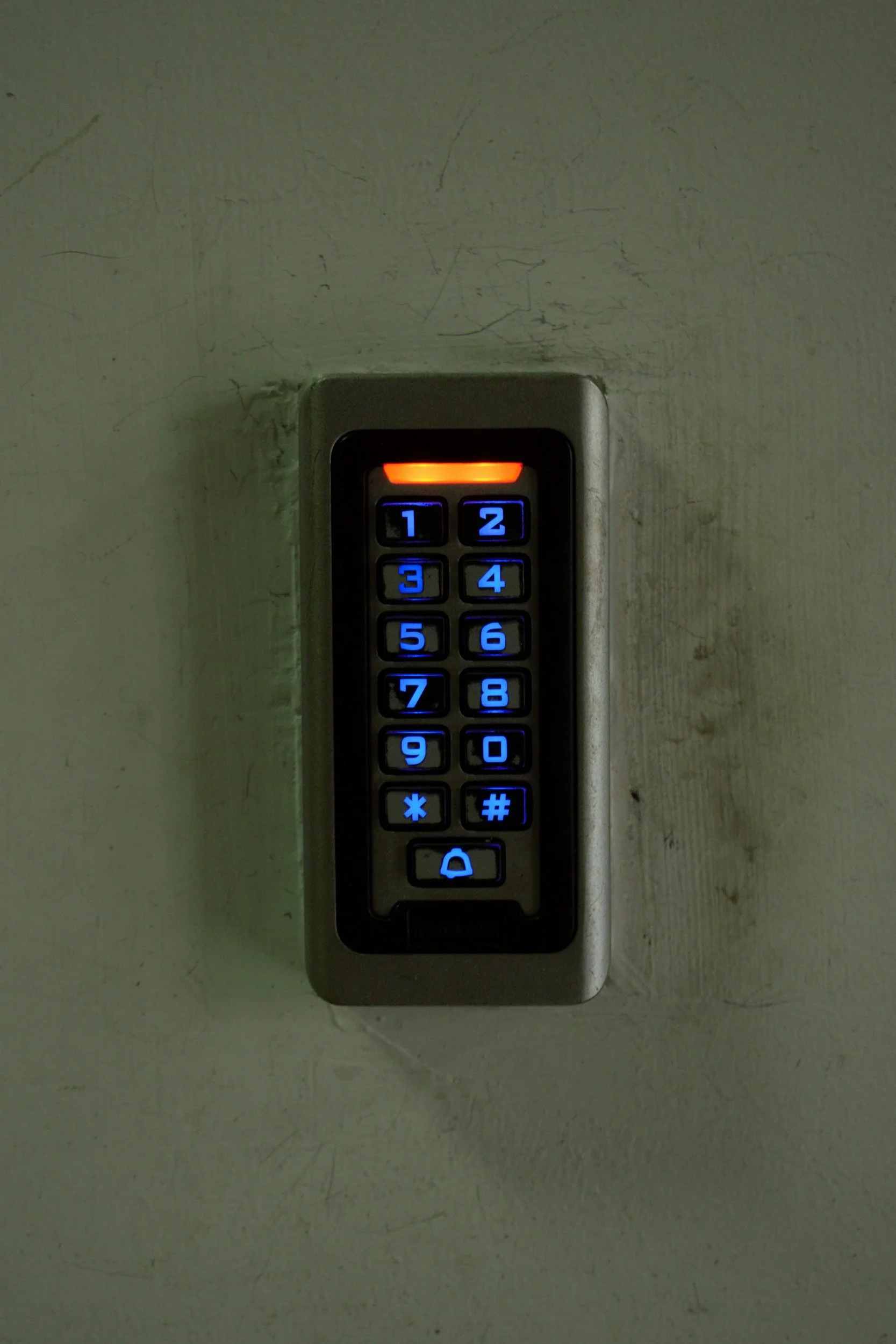 Indoor keypad lock with illuminated blue buttons on a textured off-white wall.