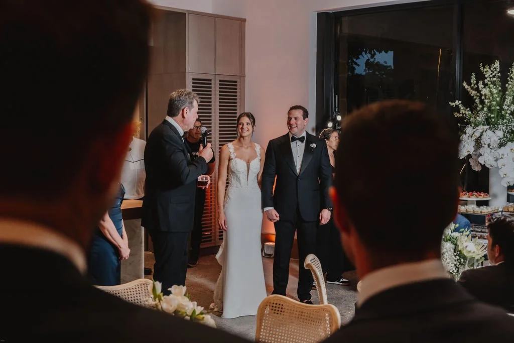 Bride and groom at their wedding ceremony, standing before guests inside a decorated venue.