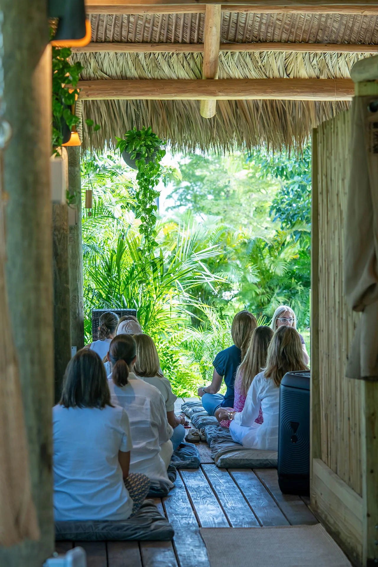 A woman practicing yoga outdoors on a yoga mat, performing a low lunge pose with arms raised overhead, surrounded by trees and natural scenery.