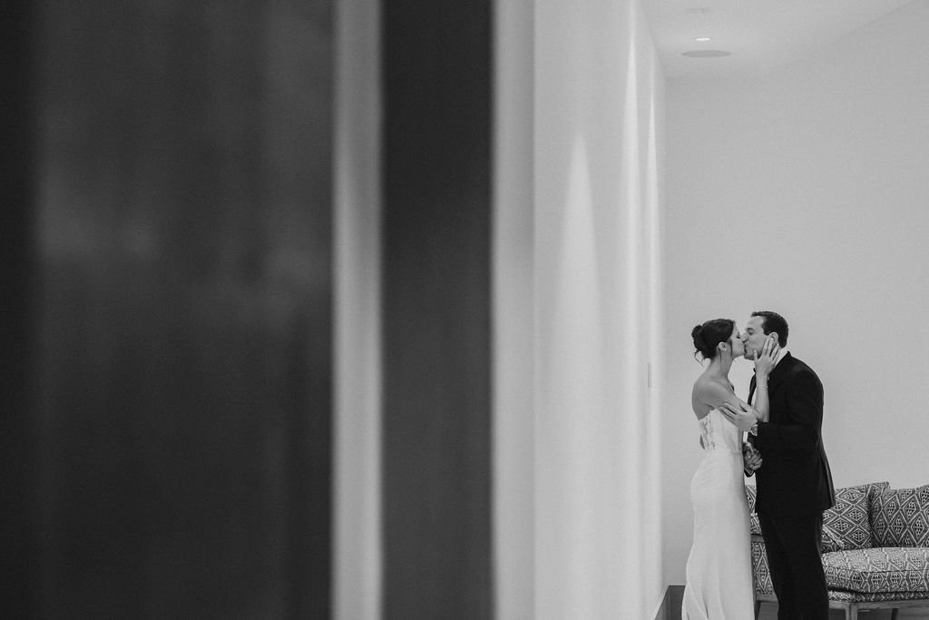 A couple sharing a kiss in a minimalistic room, with patterned sofa beside them, black and white photo.
