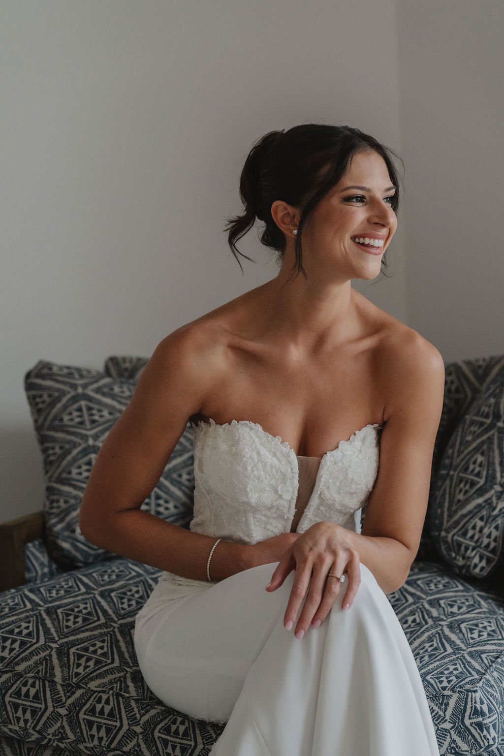 A smiling woman in a wedding dress sitting on a patterned couch.
