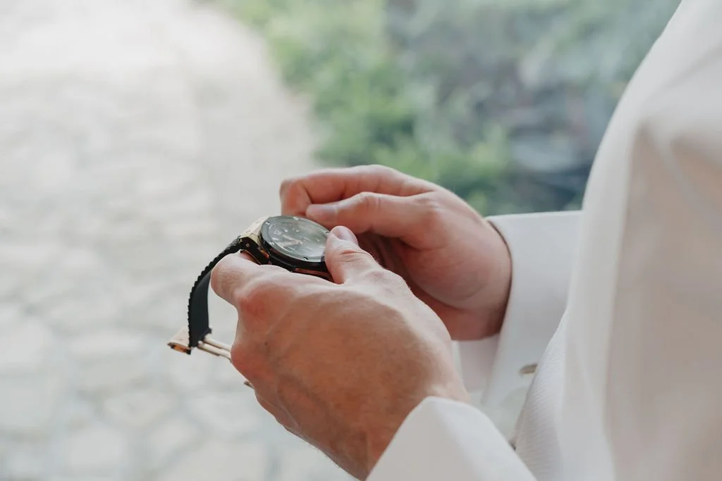 A person in a white shirt checking the time on a black wristwatch.