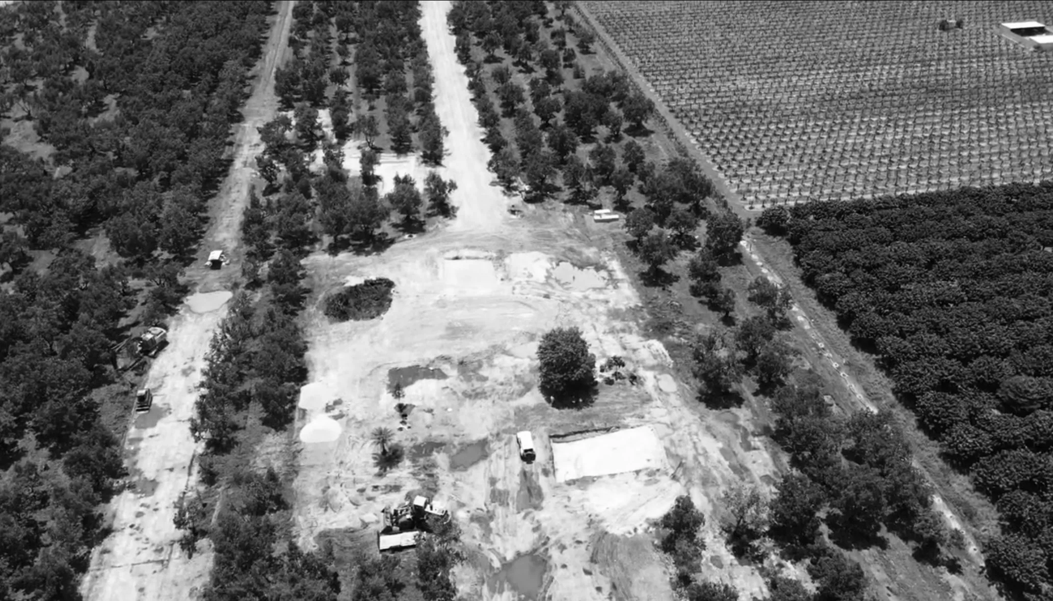 Aerial view of a construction site surrounded by trees, with dirt roads, construction vehicles, and partially built structures.