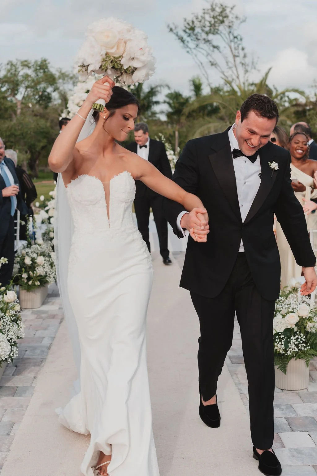 Bride and groom walking hand in hand during their wedding ceremony, smiling and celebrating outdoors with guests and floral decorations.