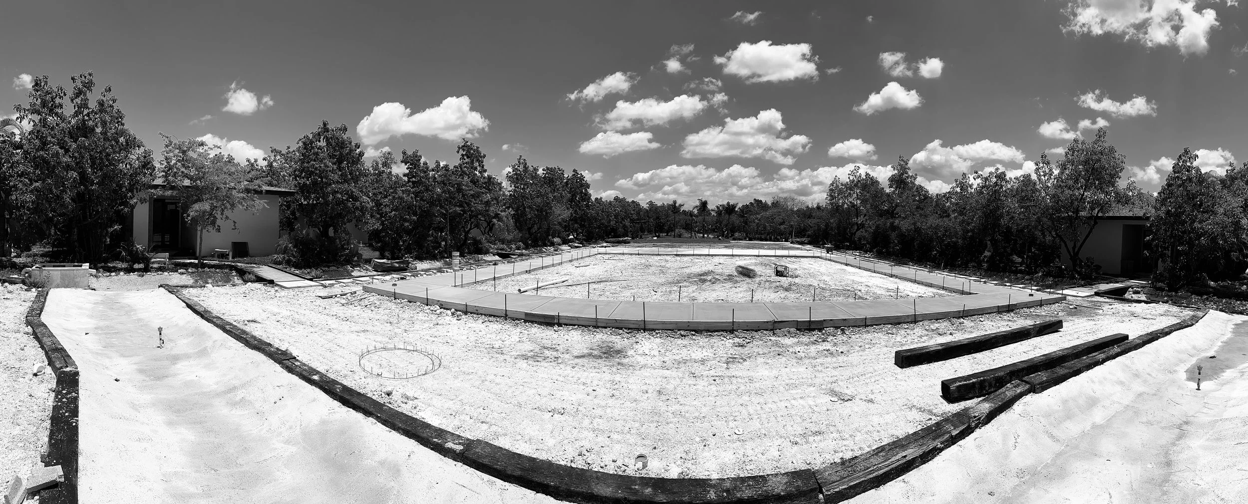 Under-construction foundation site with concrete walkways and surrounding trees under partly cloudy sky.