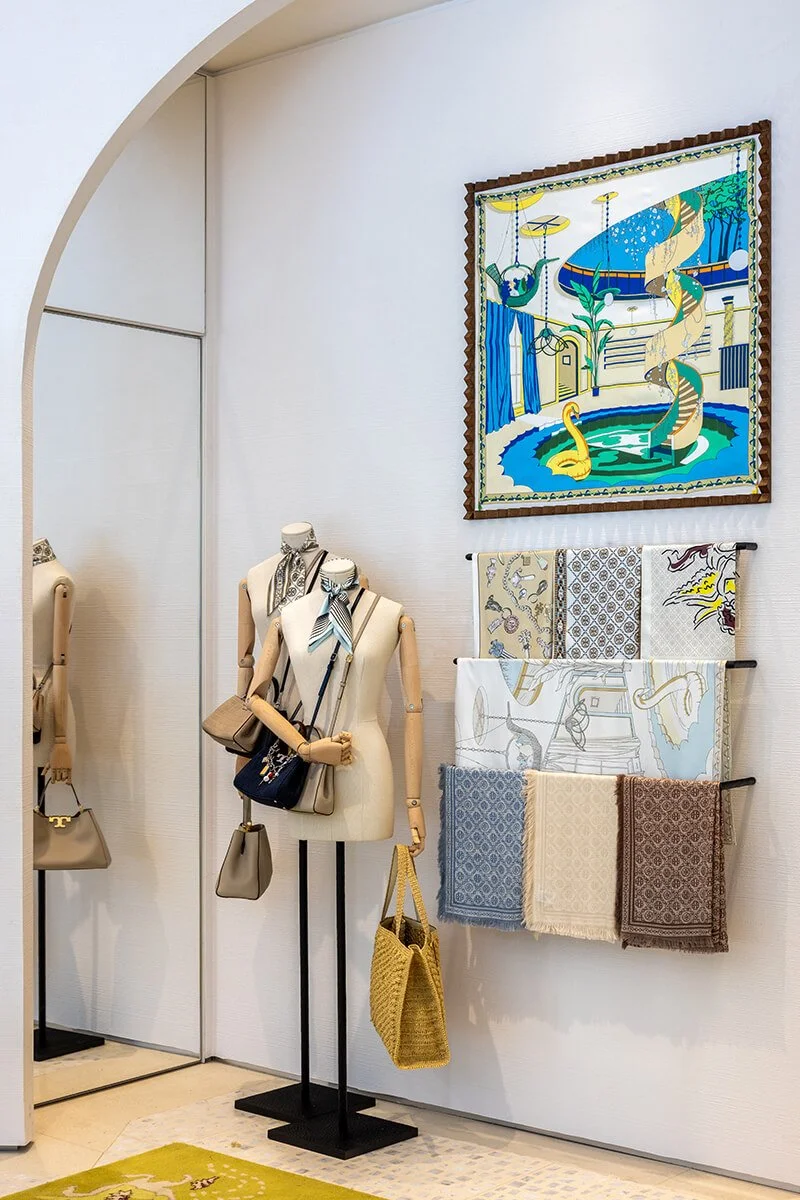 Curved wall of handbags and totes at the Tory Burch Americana Manhasset store, styled across sculptural white shelving
