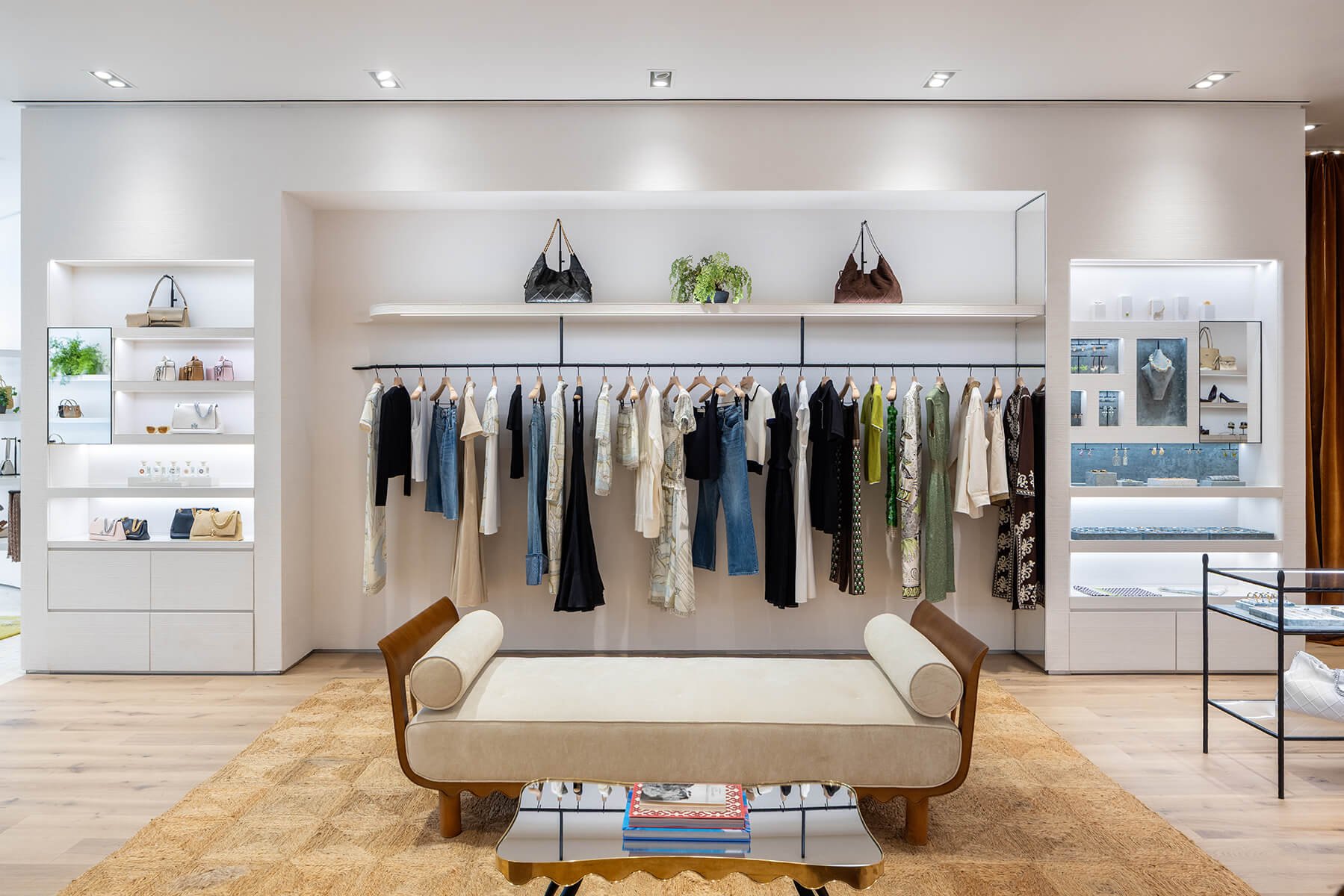Apparel wall and cream daybed at the Tory Burch Americana Manhasset store, framed by illuminated jewelry and accessory vitrines
