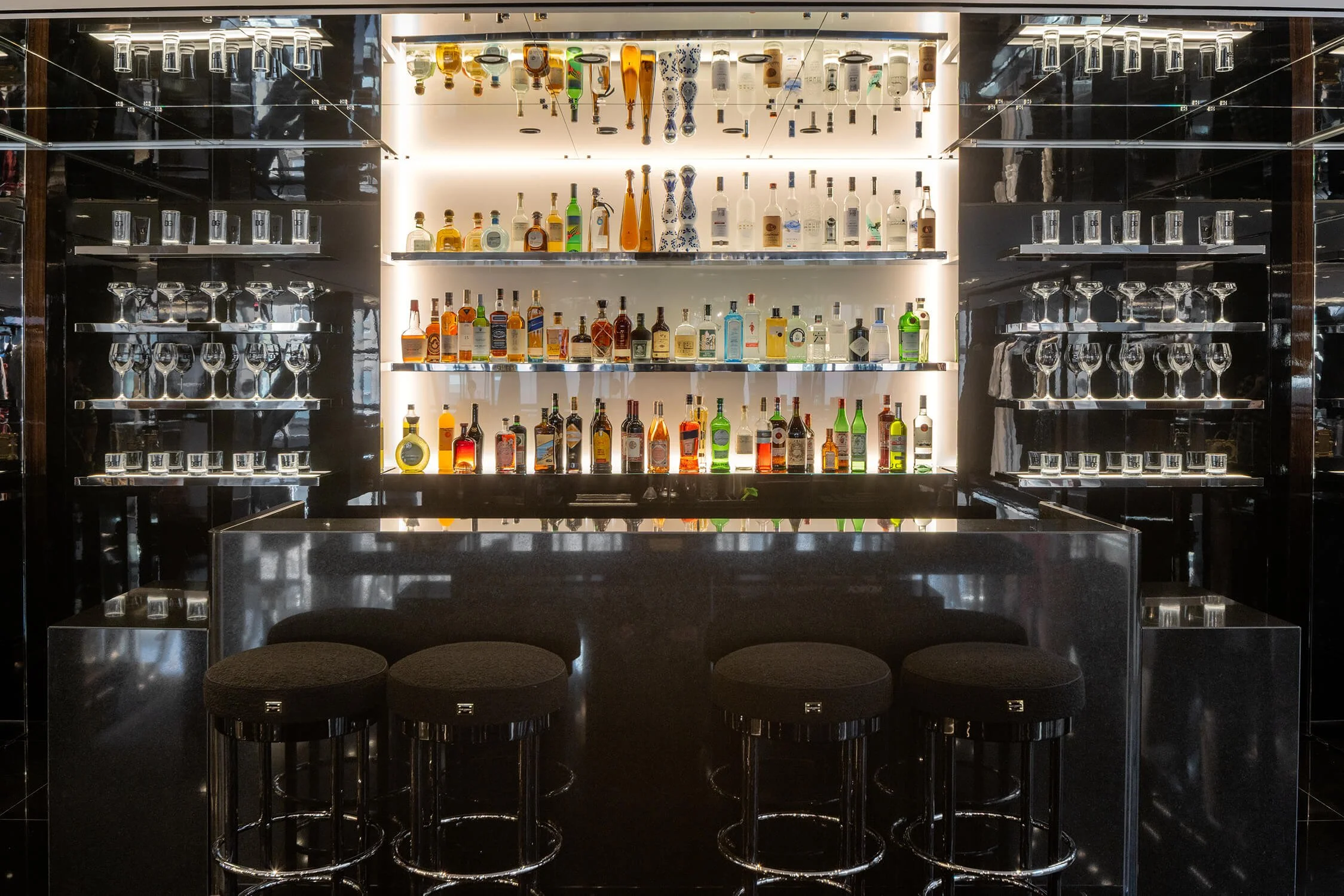 Modern in-store bar with illuminated liquor display and black seating at Dolce & Gabbana
