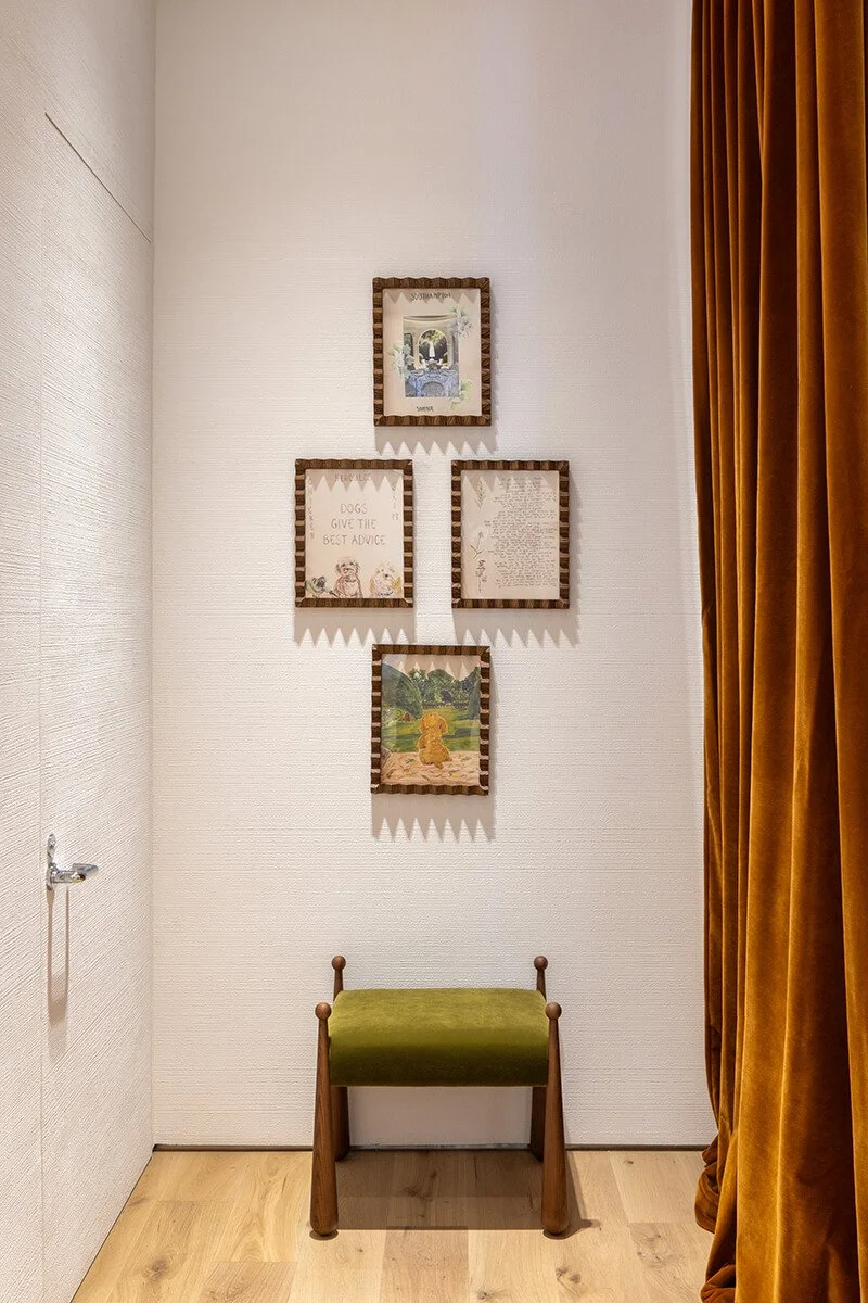Fitting area detail at the Tory Burch Americana Manhasset store, with framed dog illustrations, a green velvet stool, and a rust curtain
