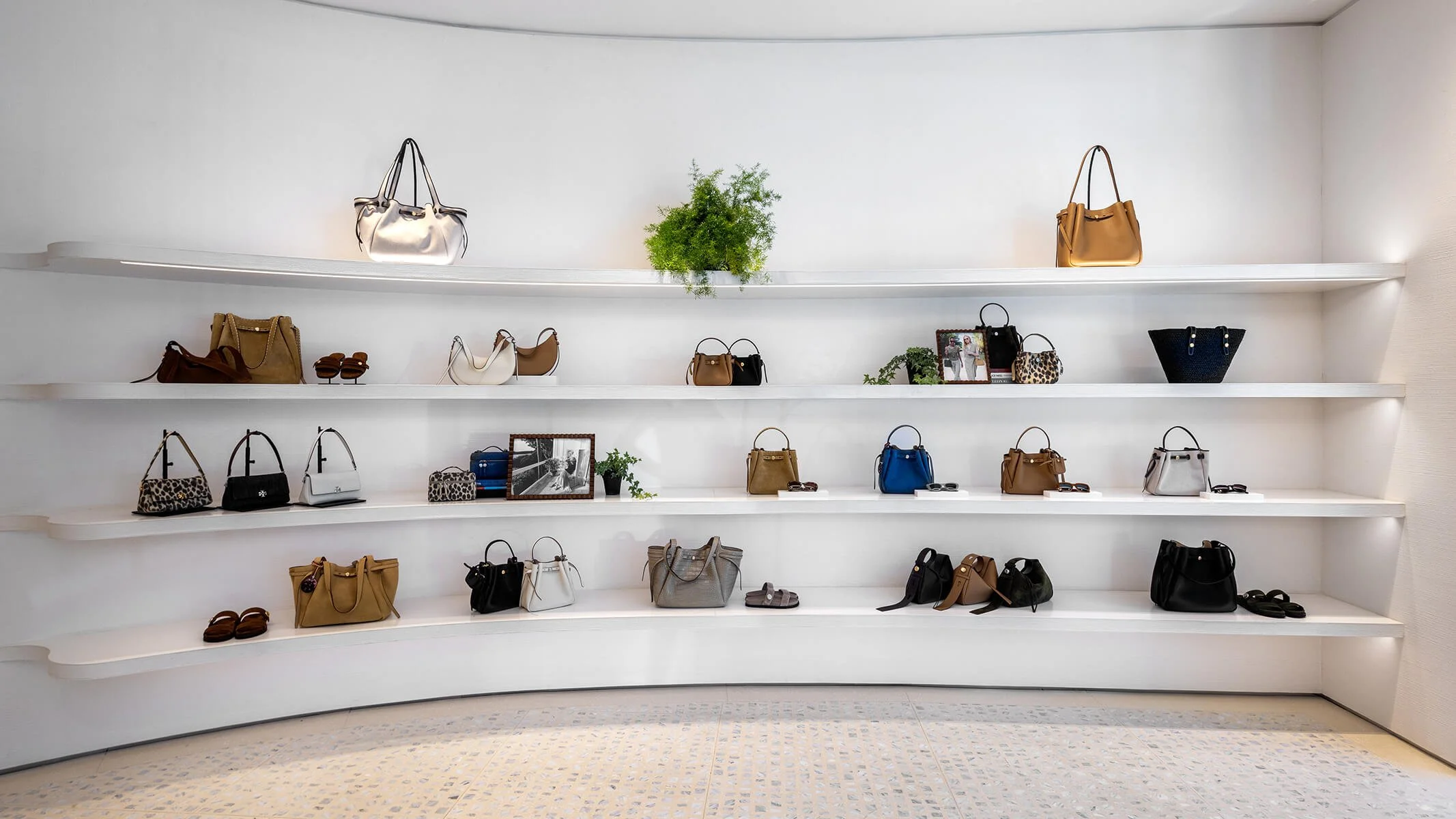 Main salon inside the Tory Burch Americana Manhasset store, with a vintage chandelier, wood daybed, and a shoe wall styled against warm oak flooring
