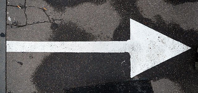 A top down photograph of a white arrow, pointing right, painted on blacktop.