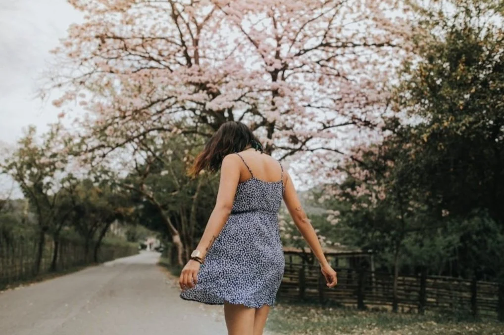 Woman walking beneath cherry blossoms from behind, reflecting identity and cultural experience, Asian American therapy in California