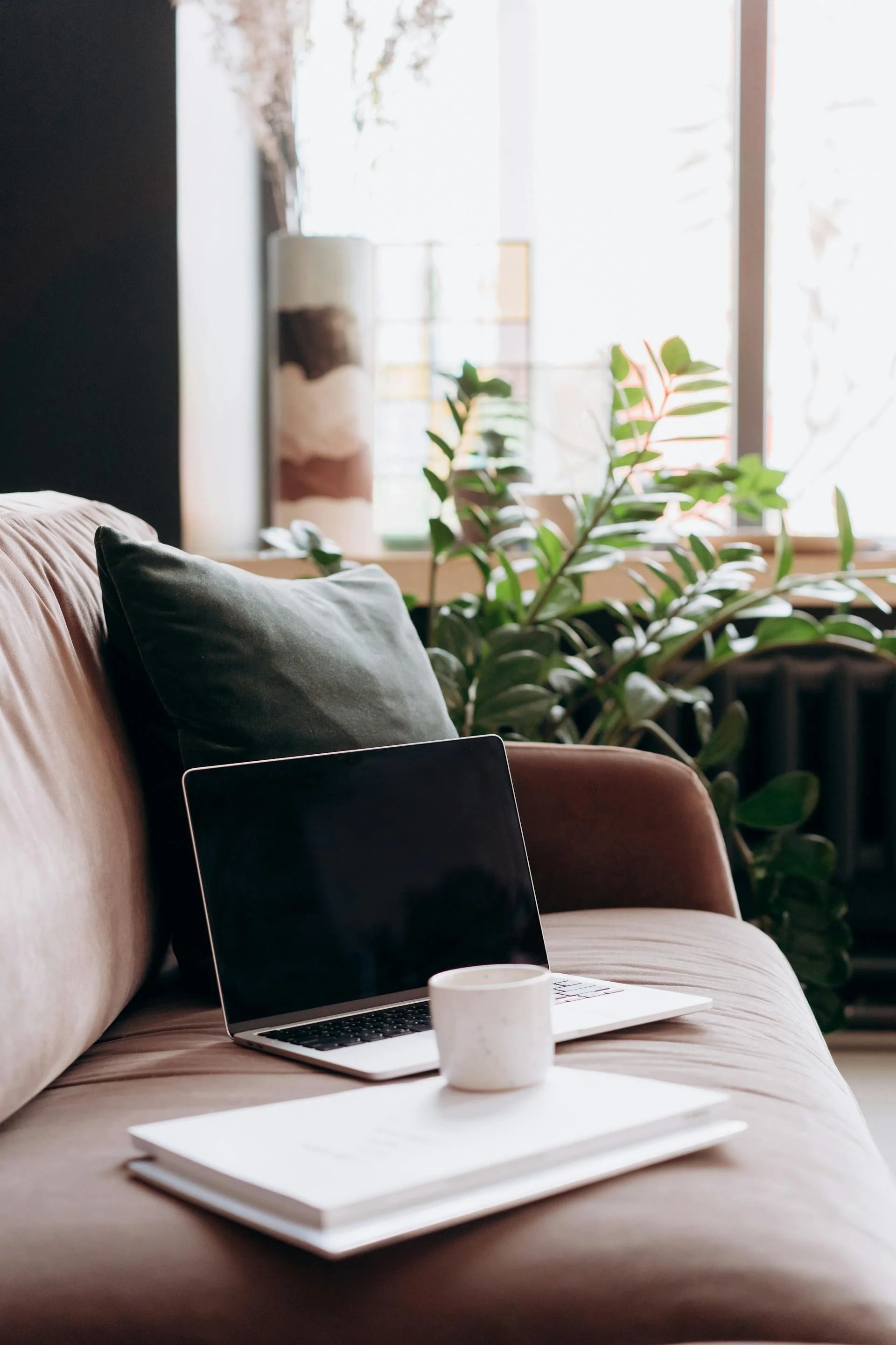 Laptop and notebook on a cozy couch with a plant, warm and supportive online therapy space