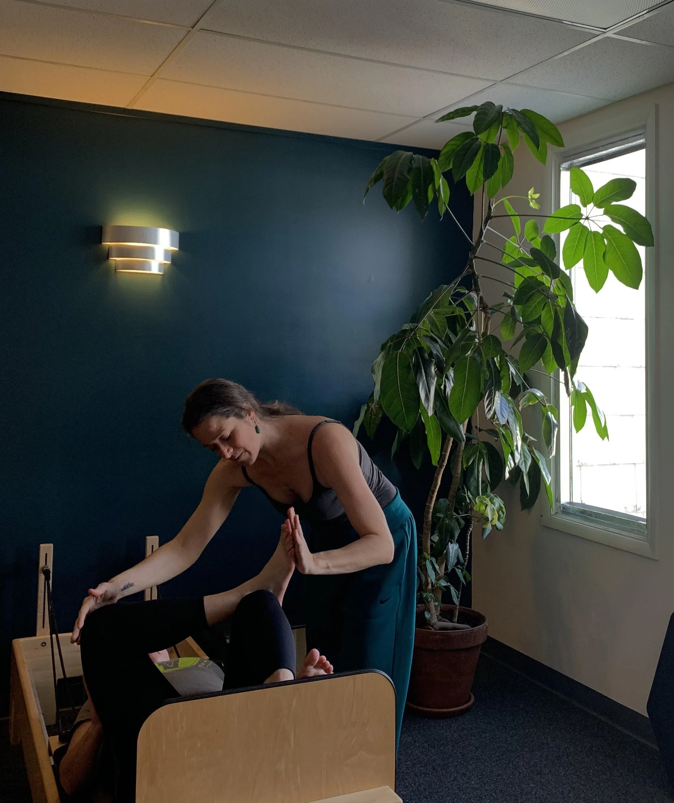 A woman assisting another person with a stretch in a Pilates studio.