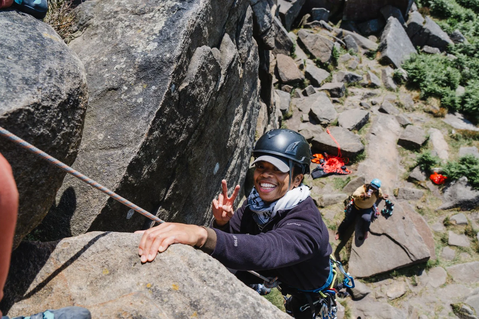 Smiling climber shows victory sign while topping out on a rock