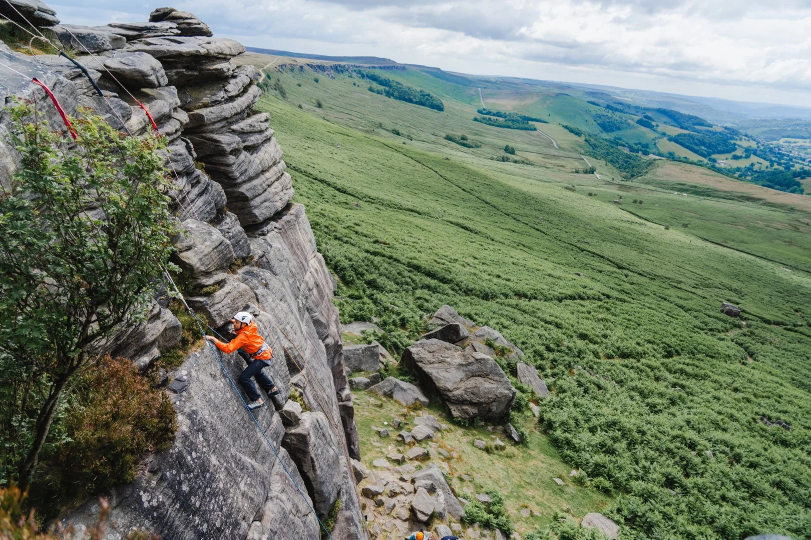 a trad climber in a bright orange jacket seen climbing on top rope