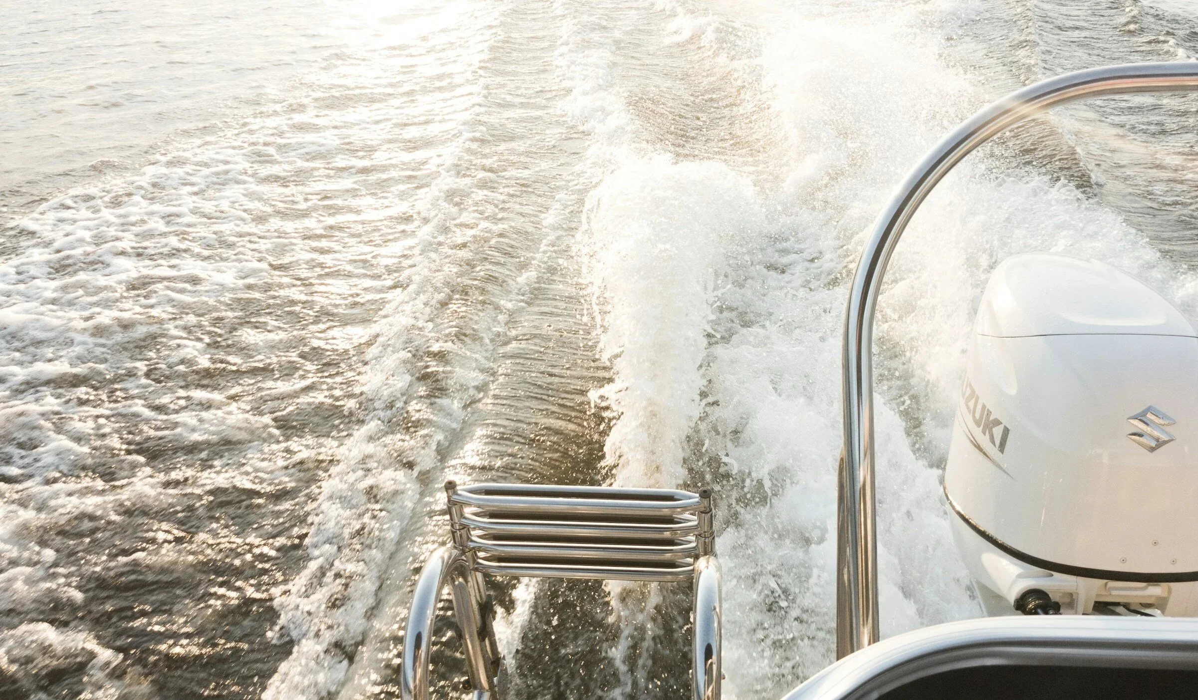 View from the back of a boat showing a Suzuki outboard motor, metal rails, and the wake created by the boat on the water.