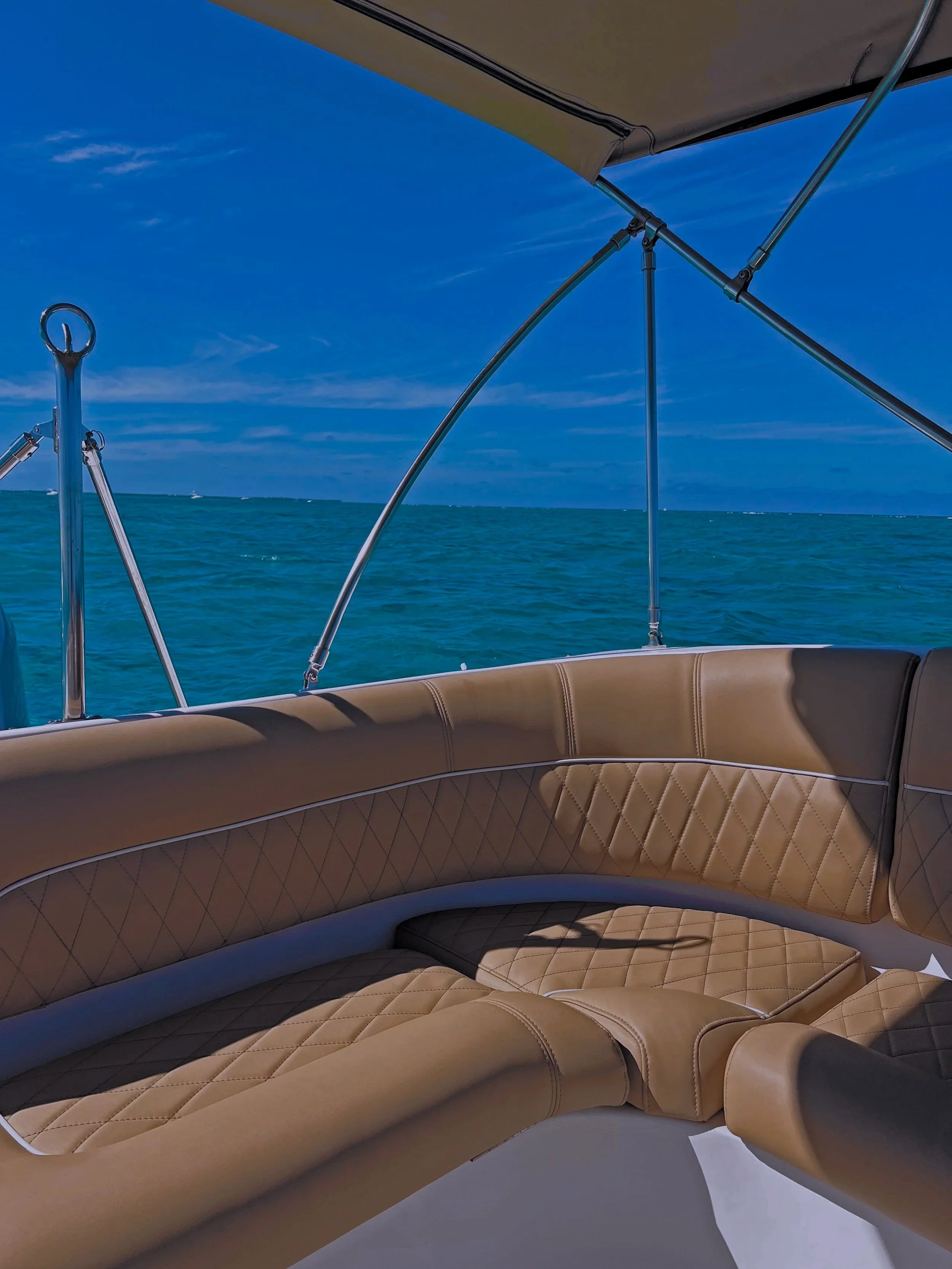 Interior of a boat with tan cushioned seating, view of the blue ocean, and a clear sky.