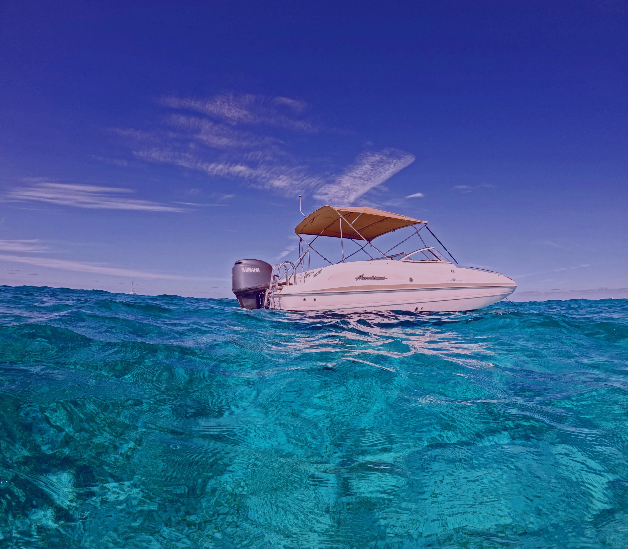 A white motorboat floating on clear blue ocean water under a partly cloudy sky.