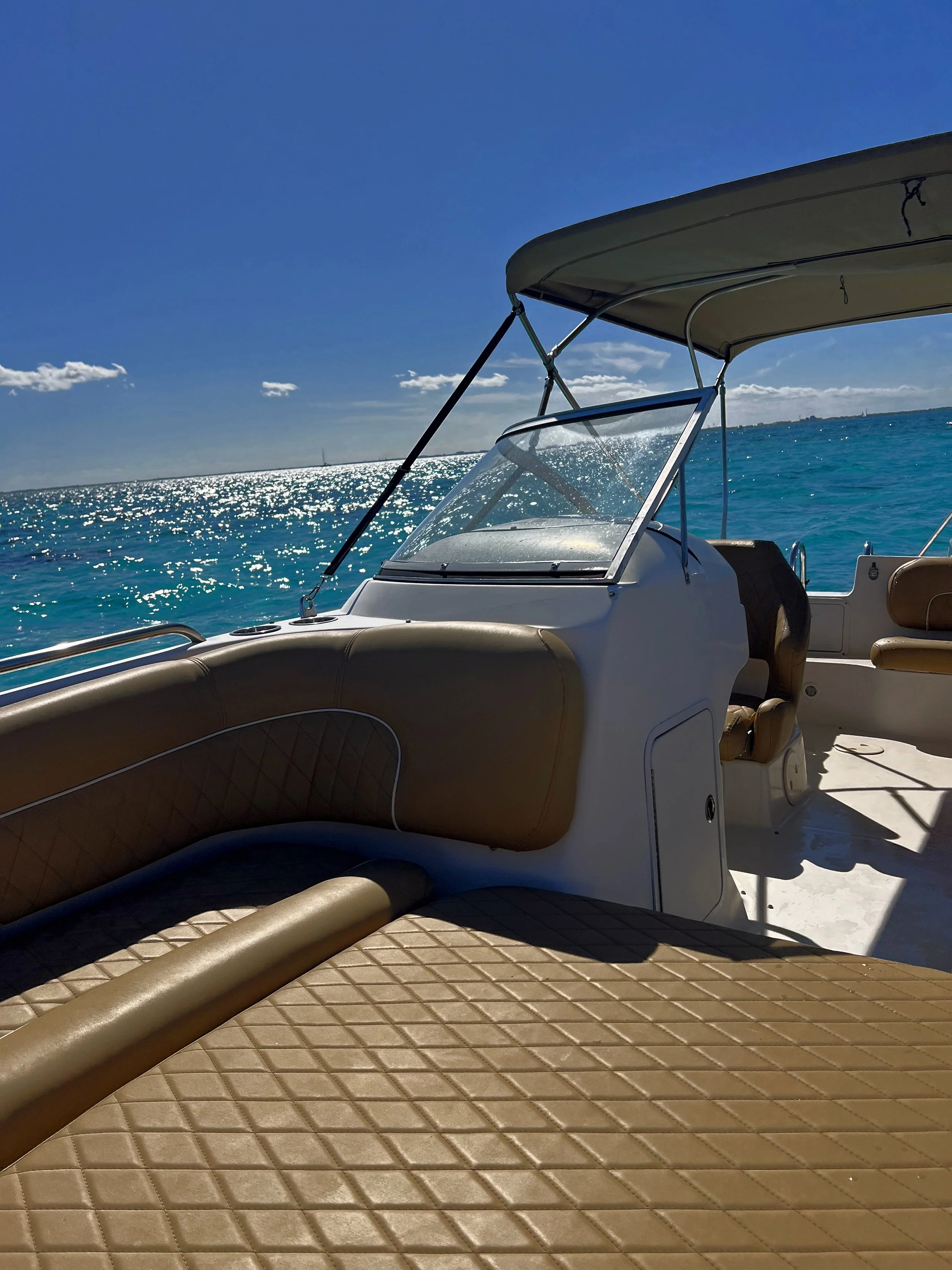 View of a boat on blue water with sunlight reflecting and a partly cloudy sky.