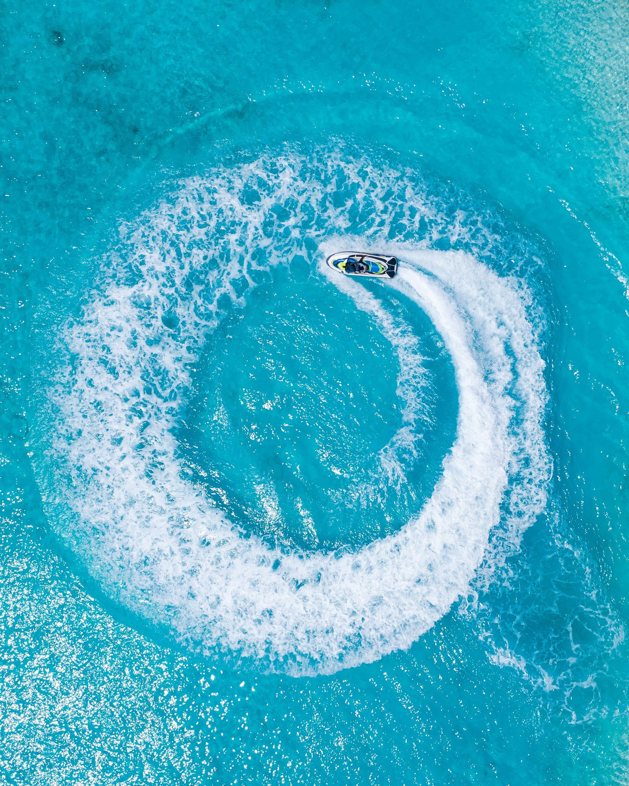 A person riding a jet ski in a spiral pattern on the water, leaving a trail of white foam in a large circular shape.