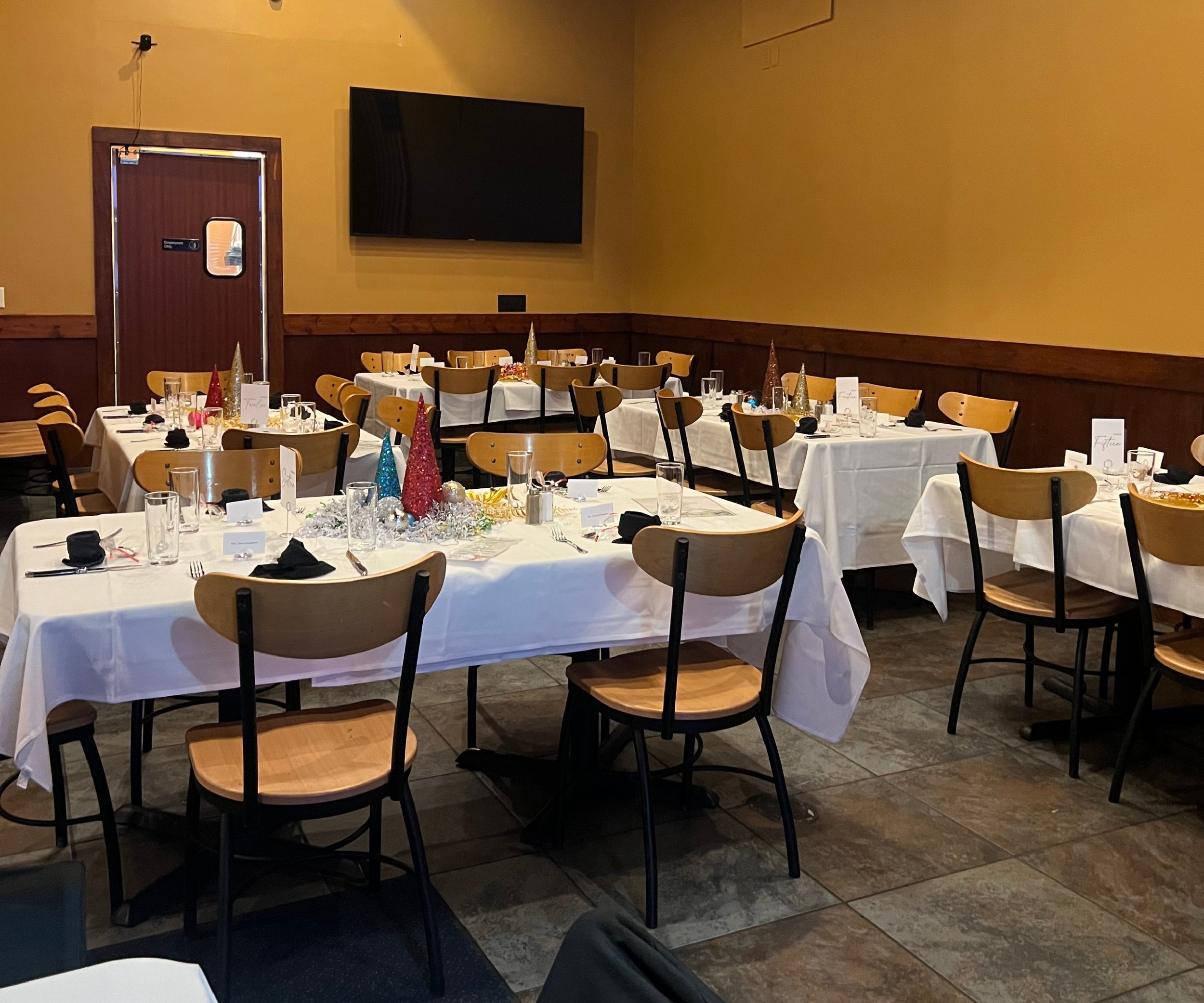 A banquet hall decorated for a holiday celebration, featuring tables with white tablecloths, colorful cone-shaped party hats, and table settings with glasses, utensils, and black napkins.