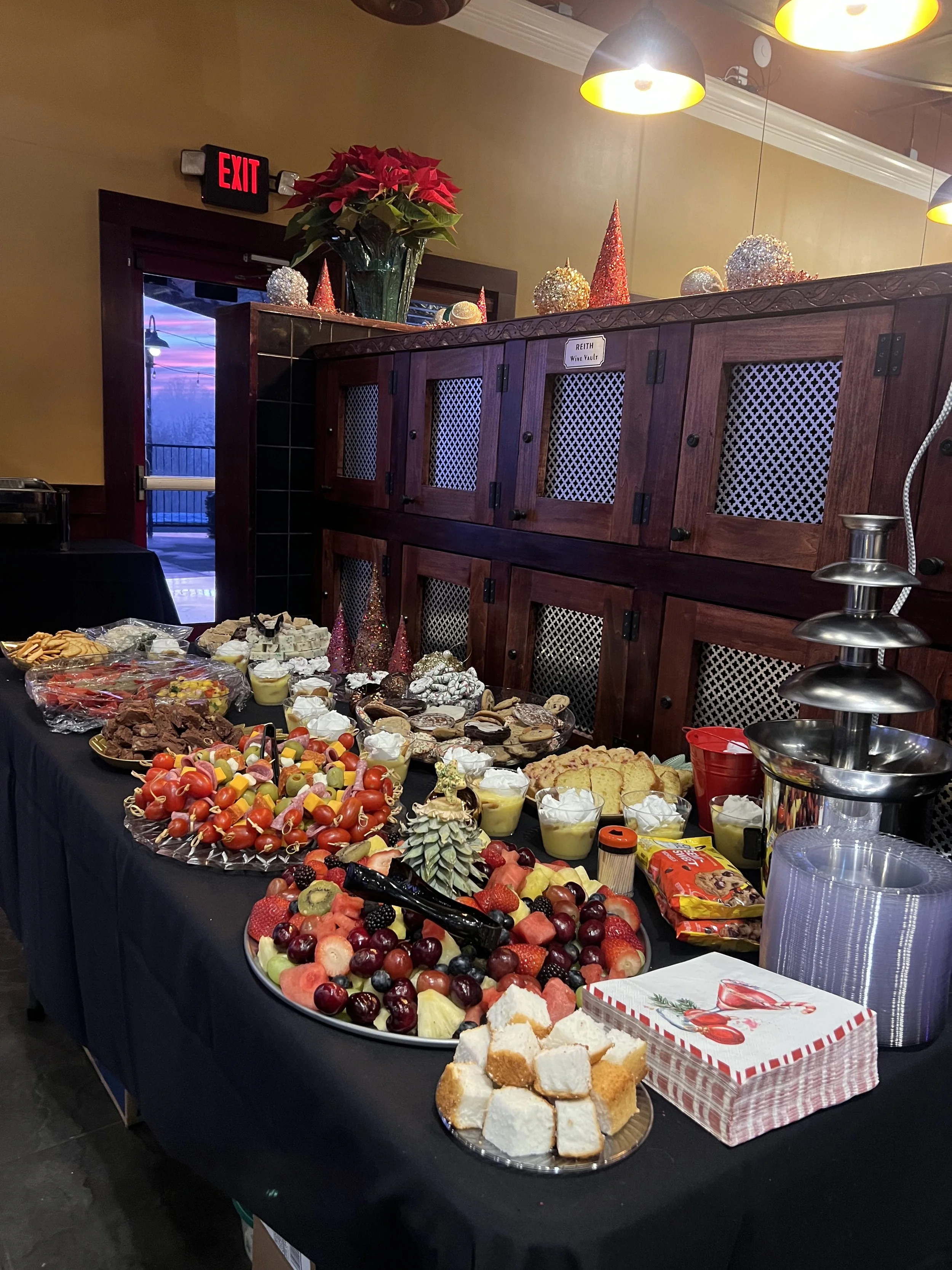 A buffet table filled with various desserts and fruit, decorated with holiday-themed ornaments on top, situated inside a restaurant with wooden cabinets and warm lighting. Host your next private event at The Copper Kettle from 2 guests to 140 guests.