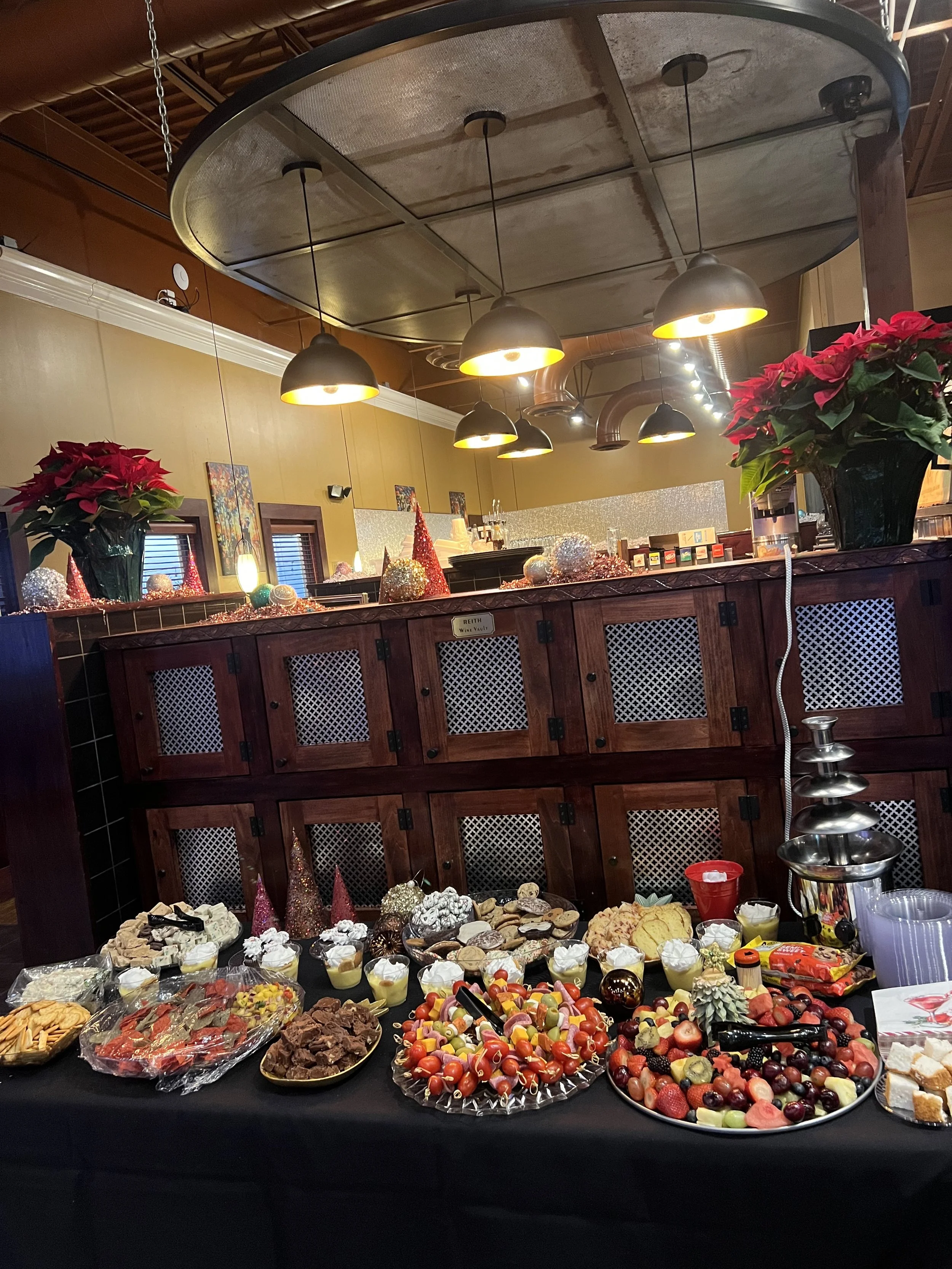 Holiday dessert and fruit platter on a black table with Christmas decorations, poinsettias, and festive ornaments behind a wooden counter in a restaurant.