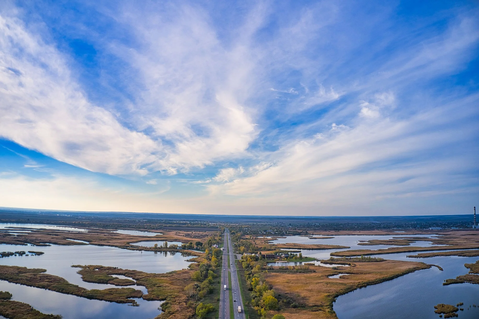 Aerial view of a road surrounded by wetlands and bodies of water under a blue sky with clouds.