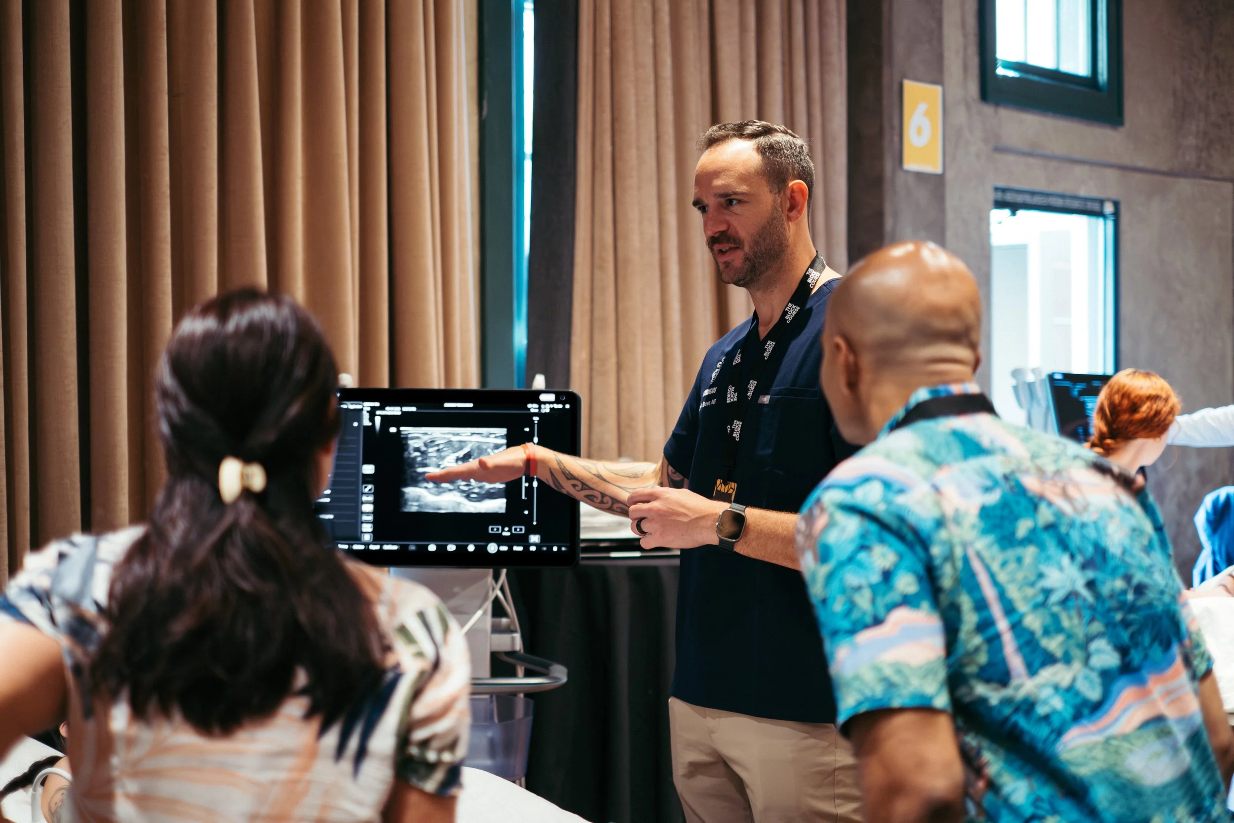 Medical professional conducting an ultrasound demonstration for a diverse group of people in a conference room.