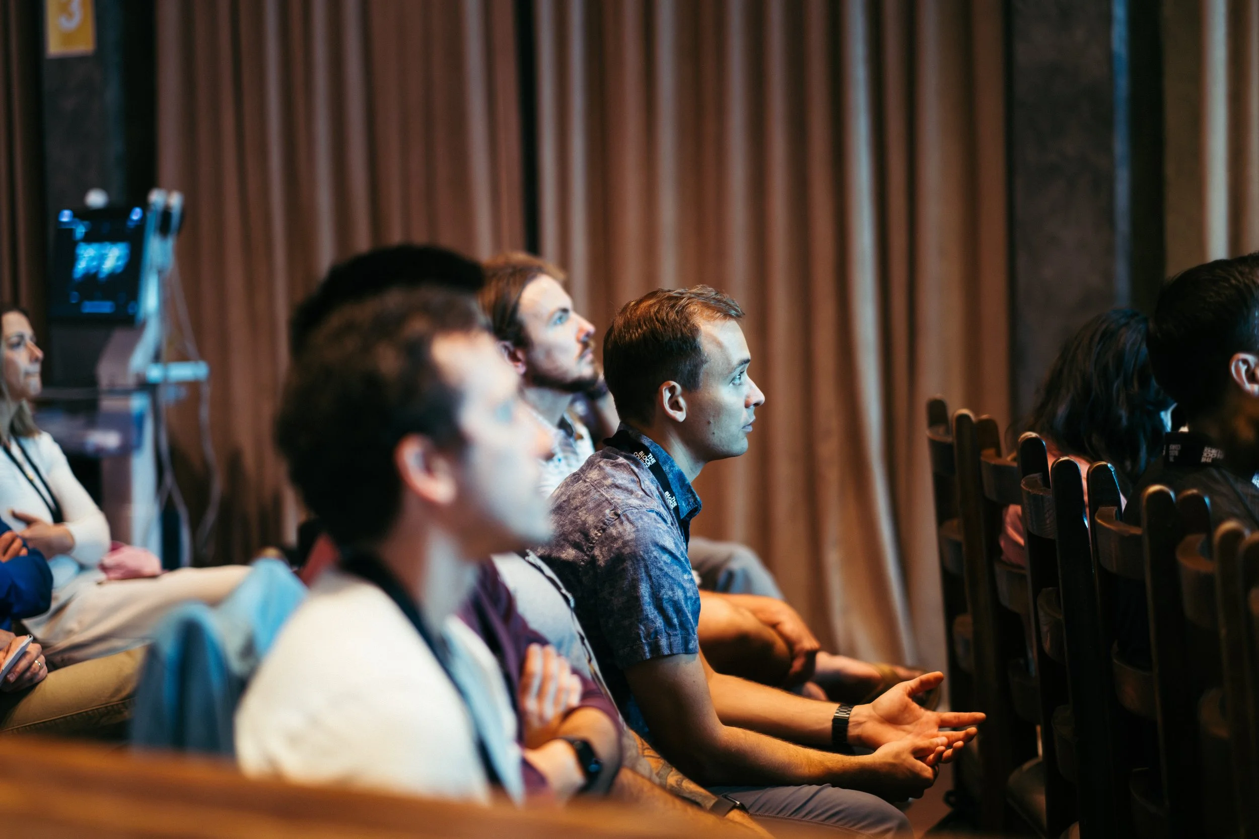 Attendees sitting in rows at a conference or seminar, focused on a speaker or presentation.