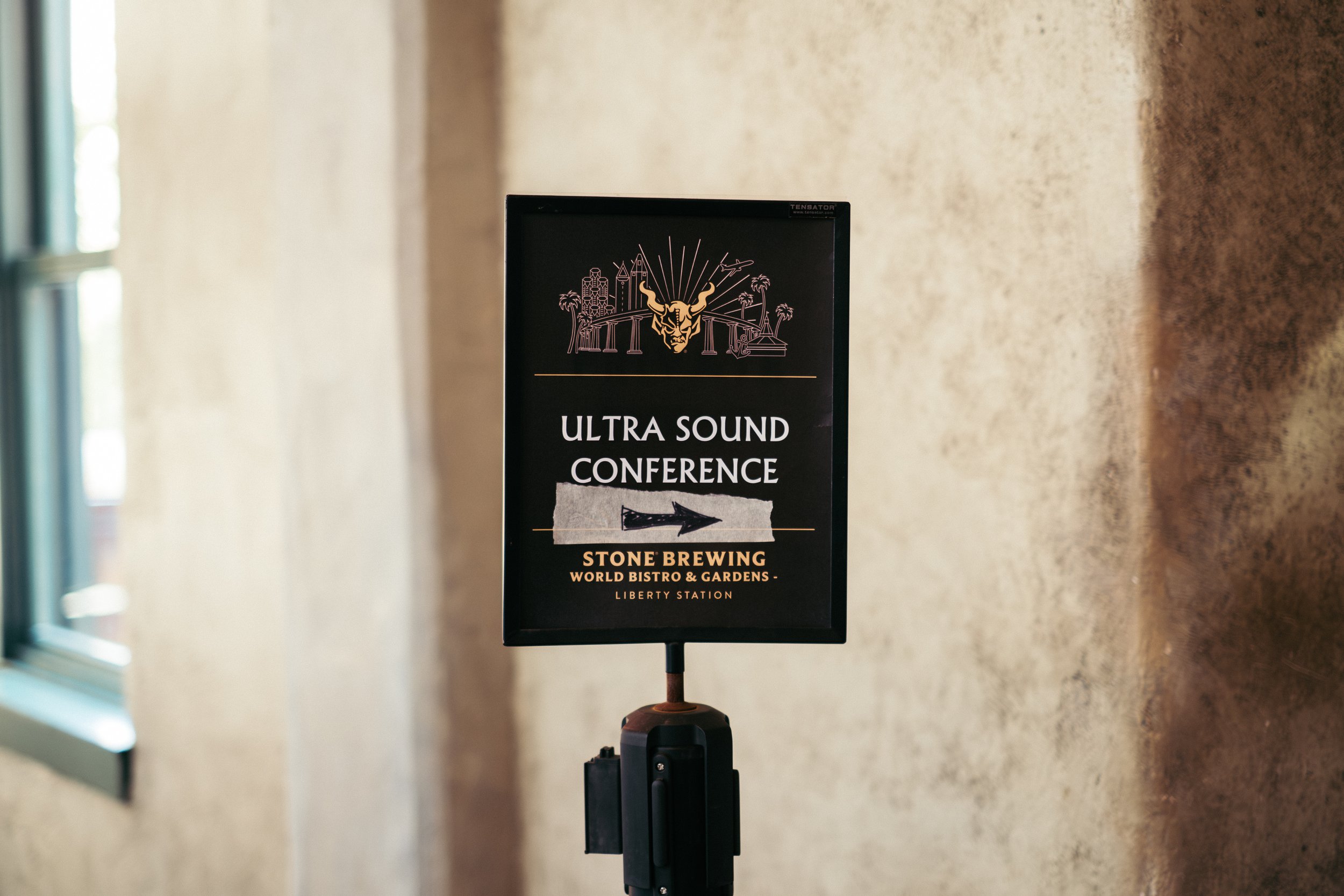 Signboard for Ultra Sound Conference, directed to Stone Brewing World Bistro & Gardens, Liberty Station, featuring a black background with gold and white text, and an illustration of a horn and buildings at the top.