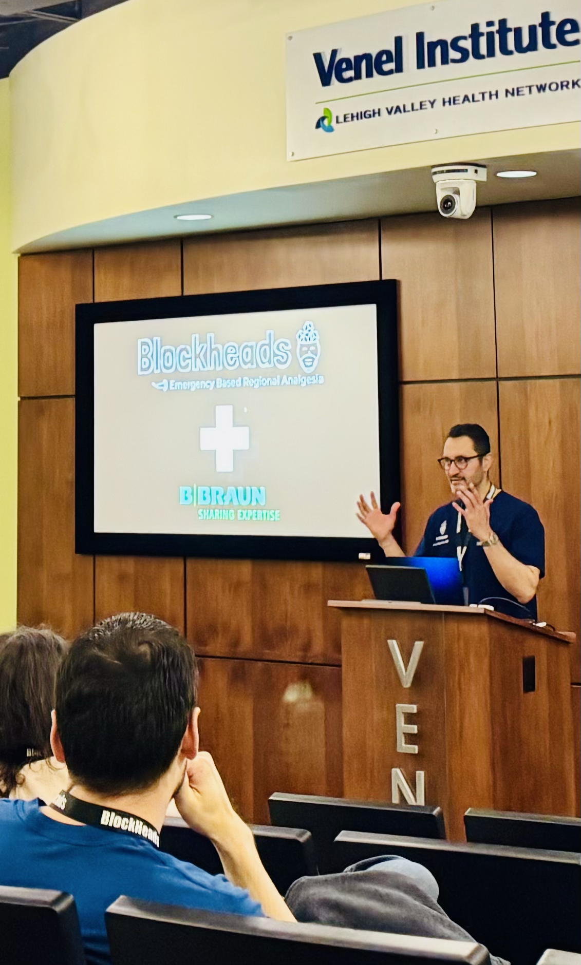 A man giving a presentation at a conference, standing behind a podium with 'VEN' visible vertically. The slide on the screen reads 'Blockheads Emergency Based Regional Analgesia' and features logos for 'Lehigh Valley Health Network' and 'B. Braun Sha