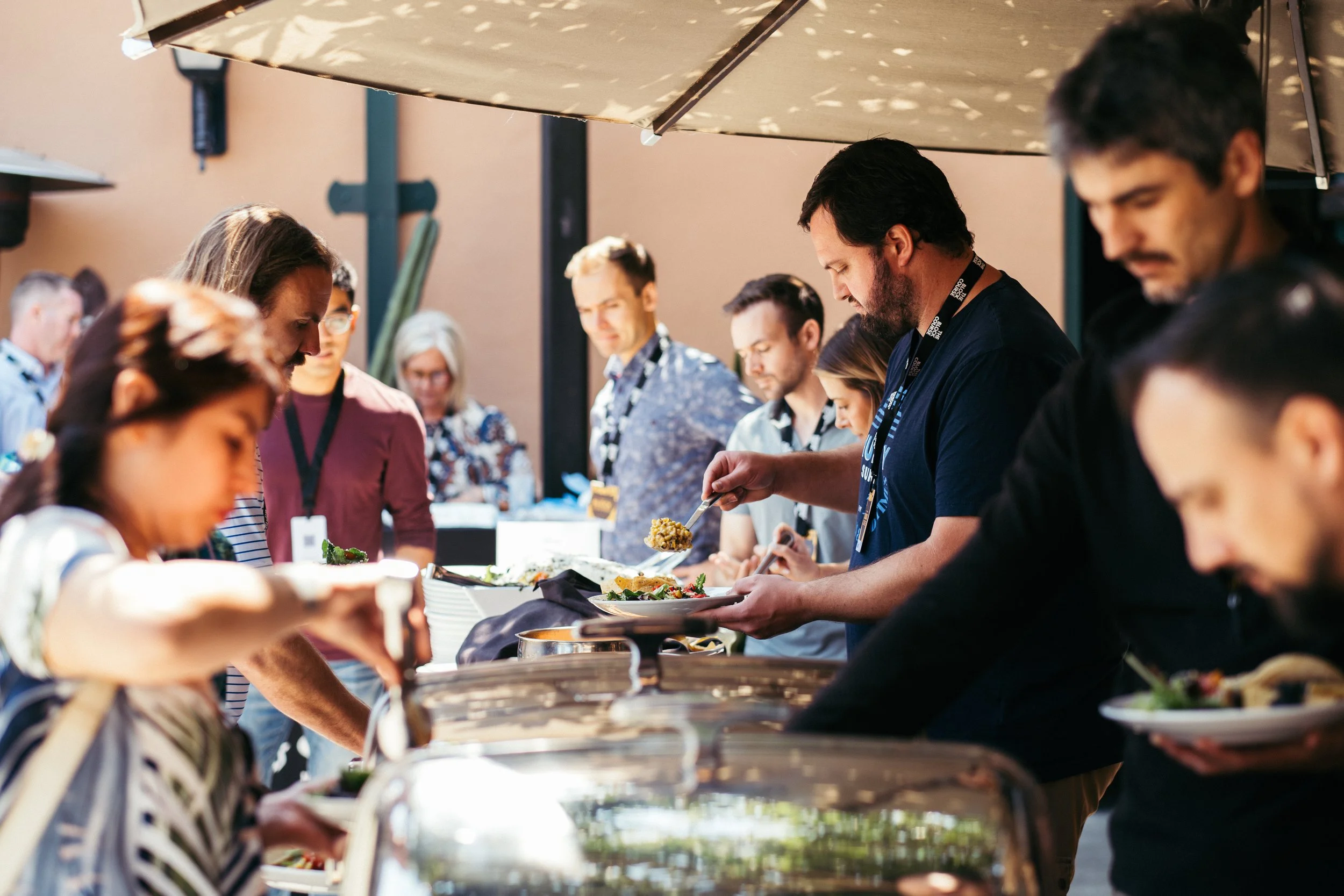 People serving themselves food at a buffet table outdoors during daytime.