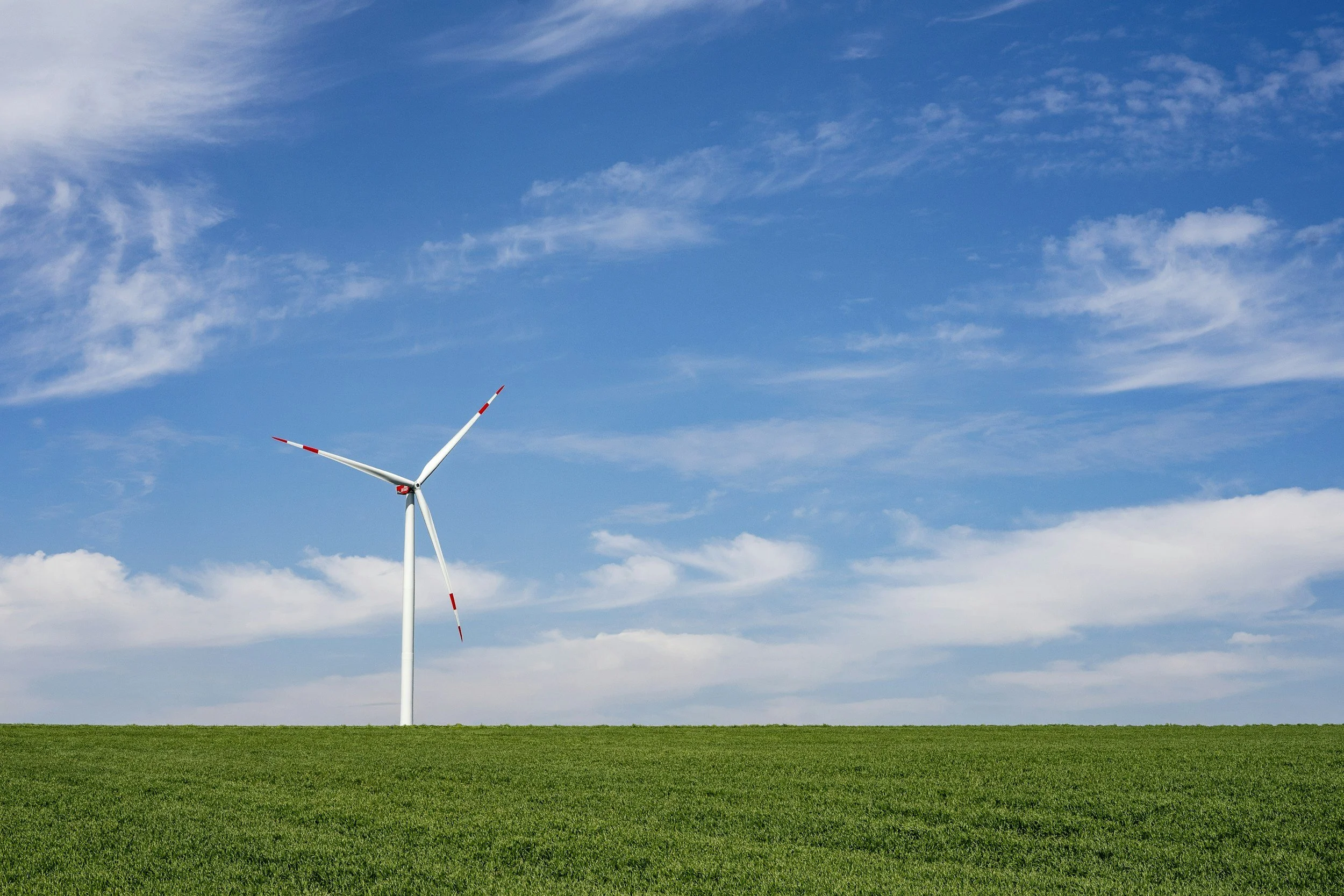 Wind turbine in a green field under a blue sky with clouds.