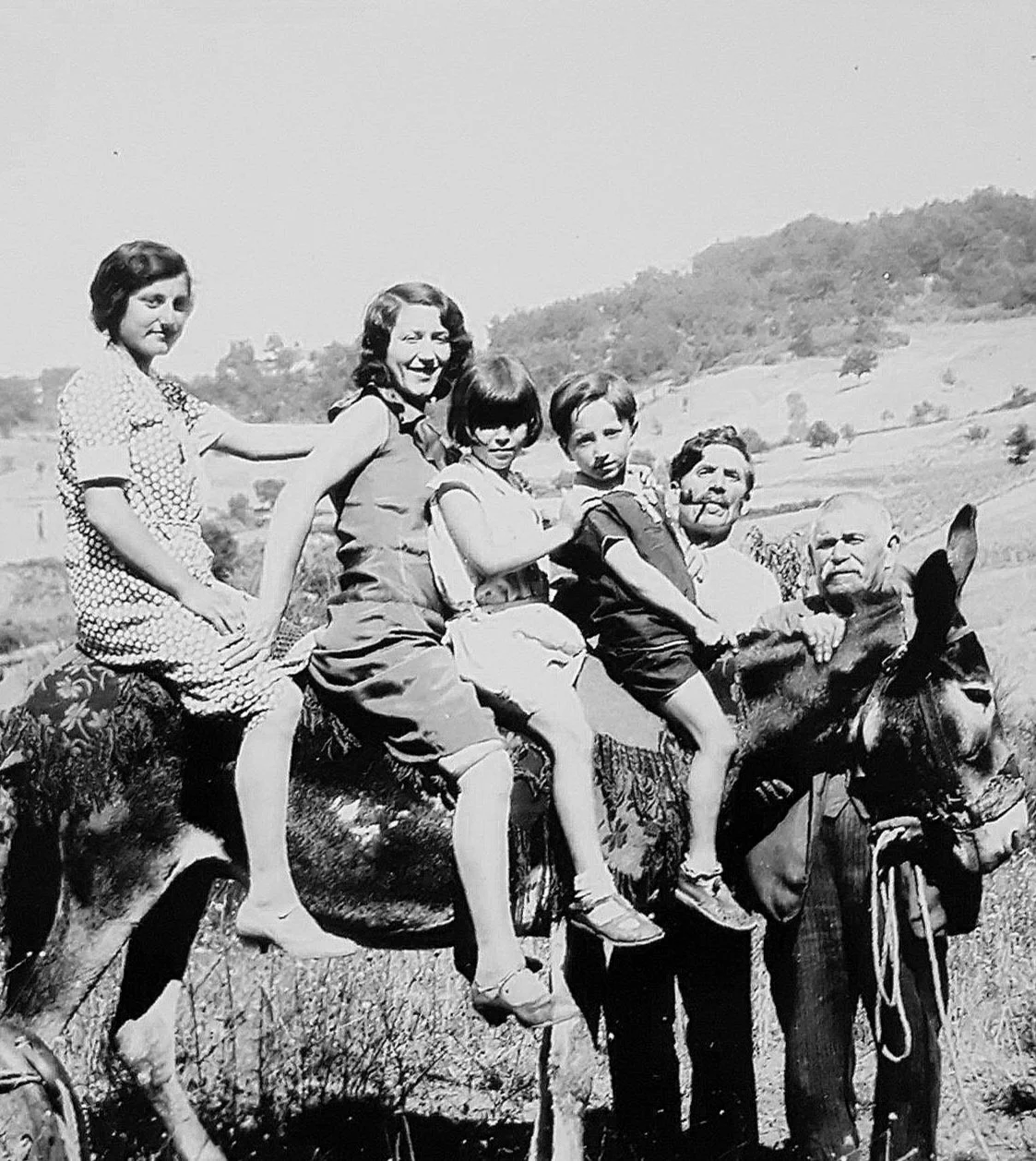 Black and white photo of a family riding a donkey, with five children and an adult man, in a rural landscape.