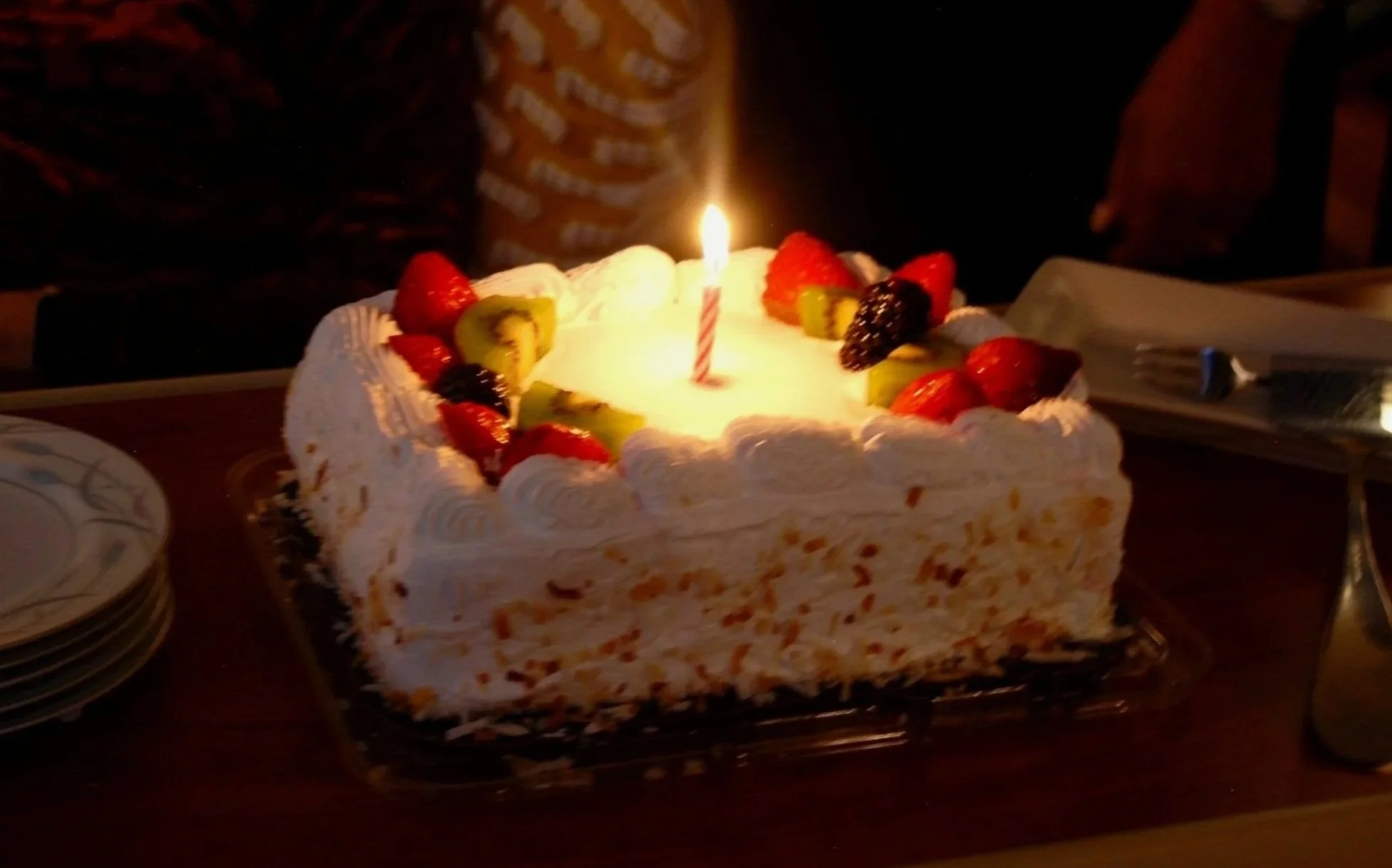 A birthday cake decorated with strawberries, kiwi, and blackberries, topped with a lit candle.