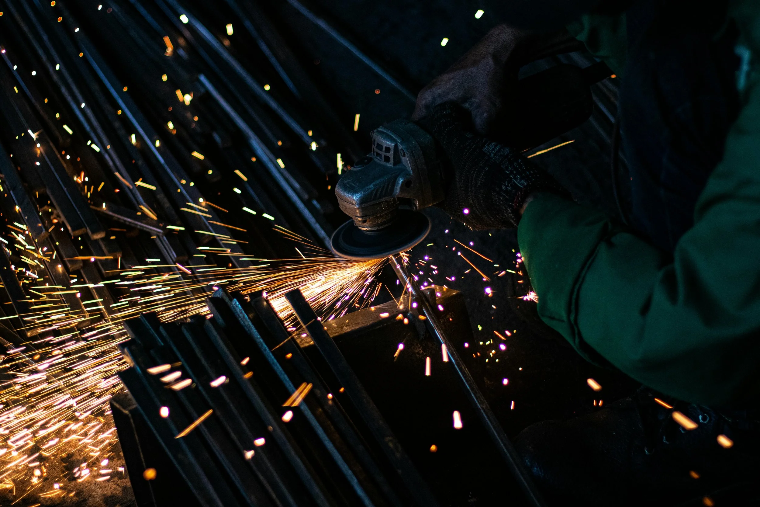 Worker using an angle grinder to cut metal, creating sparks.