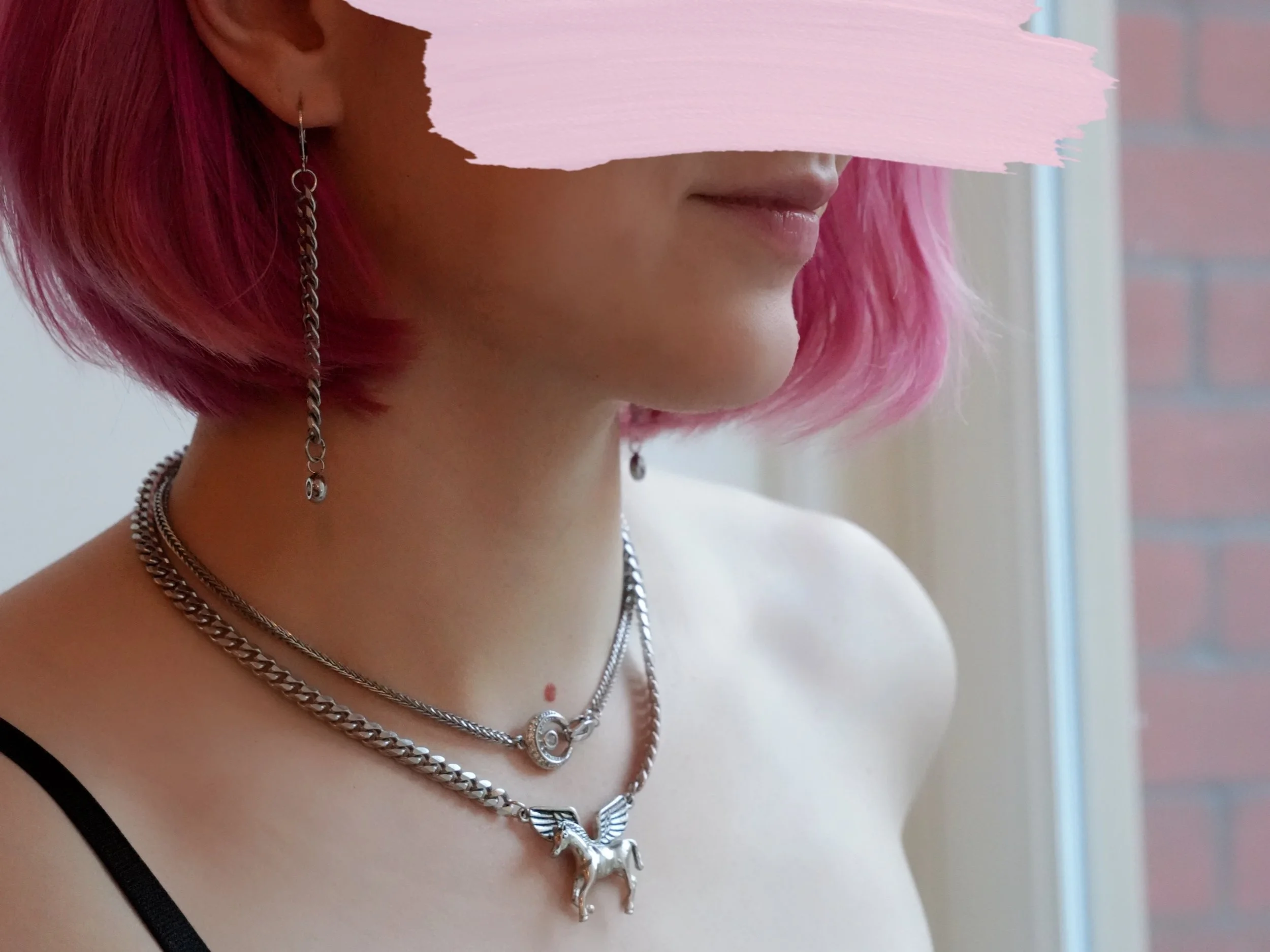 Jade wears long drop earrings and two necklaces as she looks out a sunny Manhattan window. 