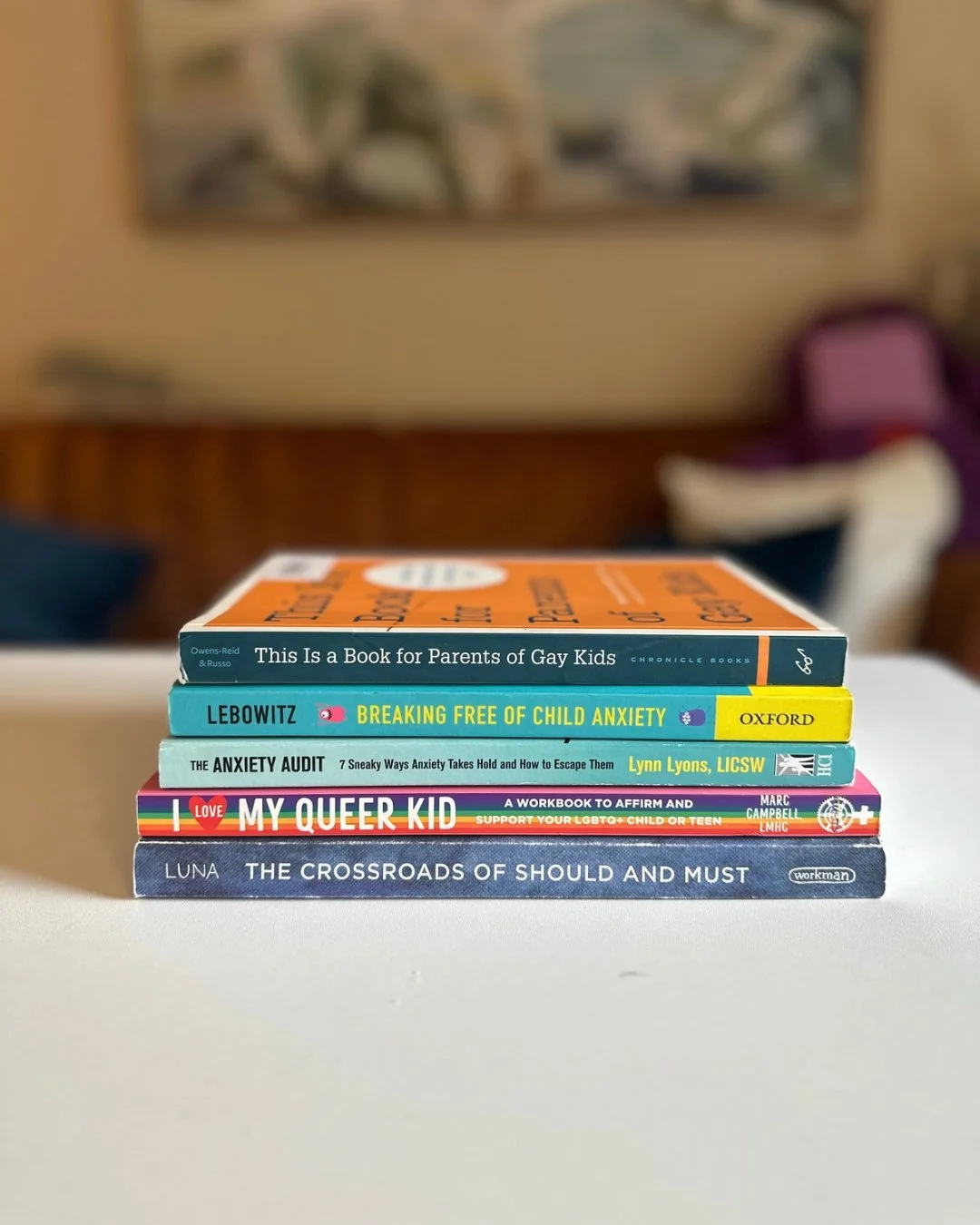 Stack of books for parents supporting LGBTQ+ children and managing child anxiety, including “This Is a Book for Parents of Gay Kids” and “I Love My Queer Kid.”