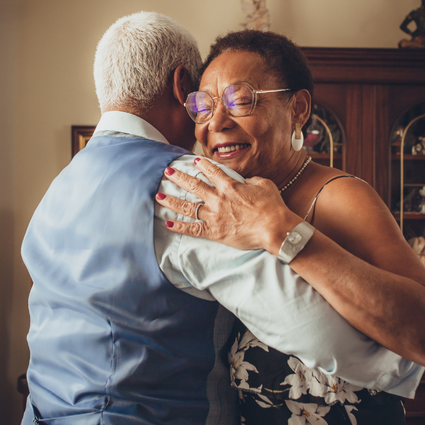 An elderly man and woman hugging and smiling warmly.