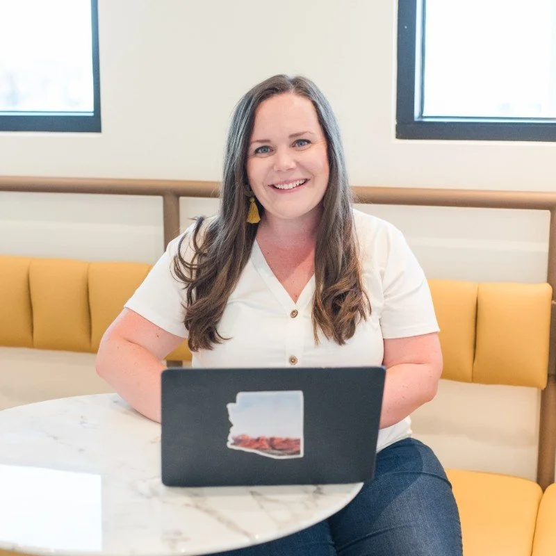 A woman sitting at a marble table using a laptop, in a cozy indoor setting with yellow cushions.