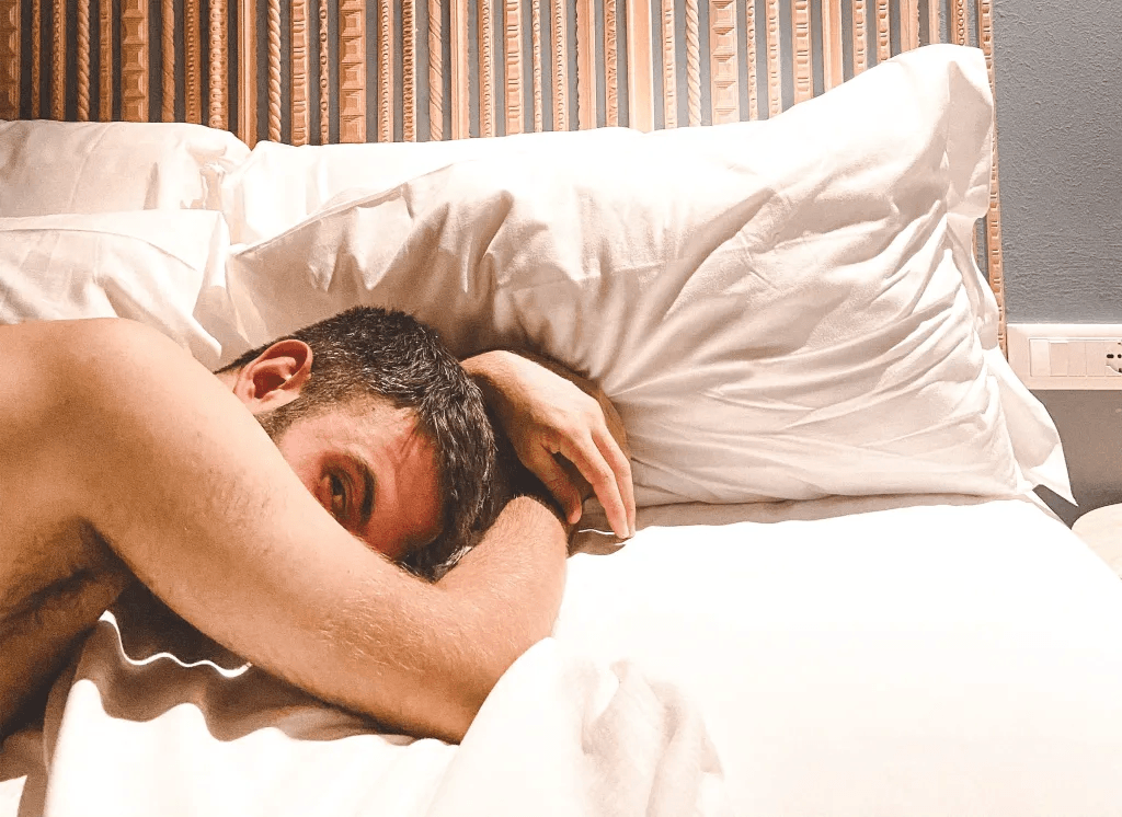A man lying on a bed with his head resting on his arm, looking towards the camera.